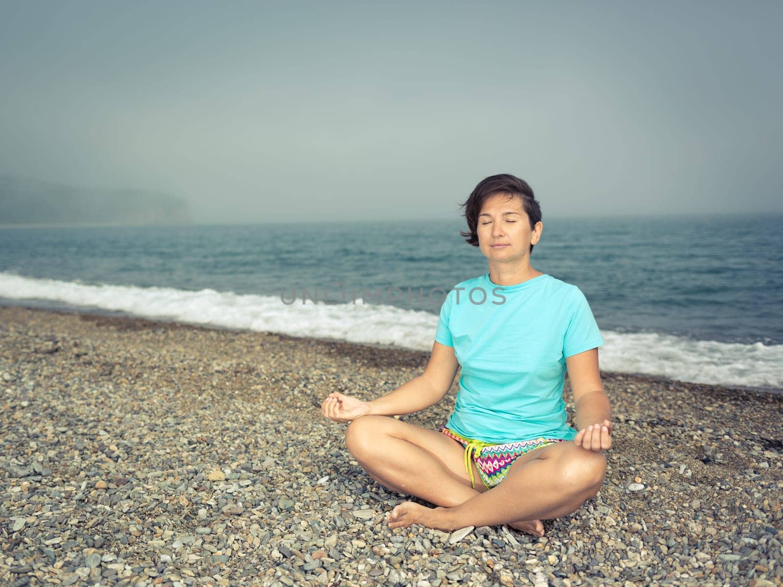 Woman meditating at seaside. Foggy weather