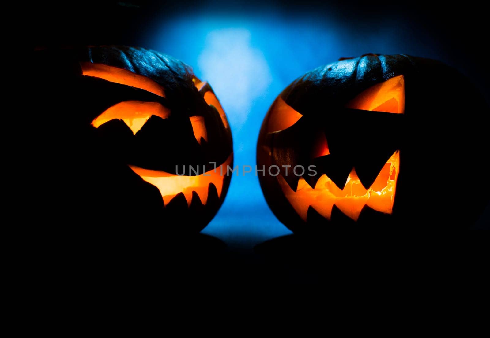 two scary halloween pumpkins on a blue light background.