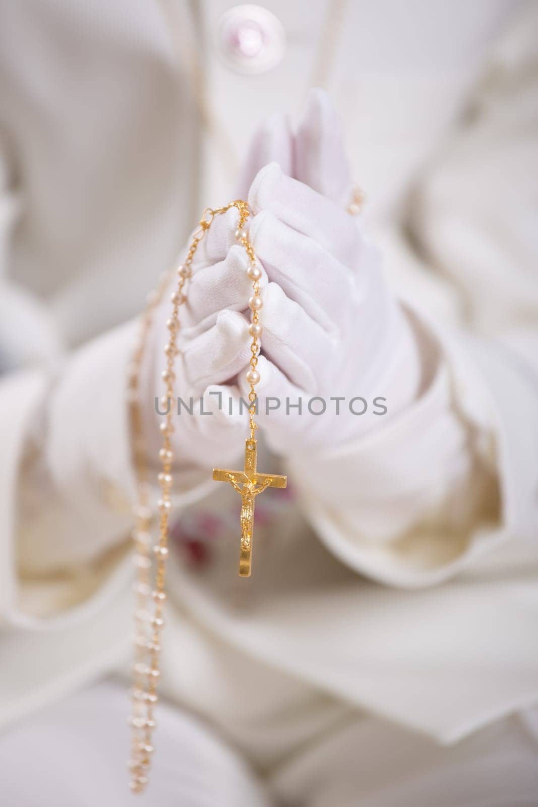 Closeup of a boy's hands with white gloves holding a gold rosary for his First Holy Communion. Shallow depth of field.