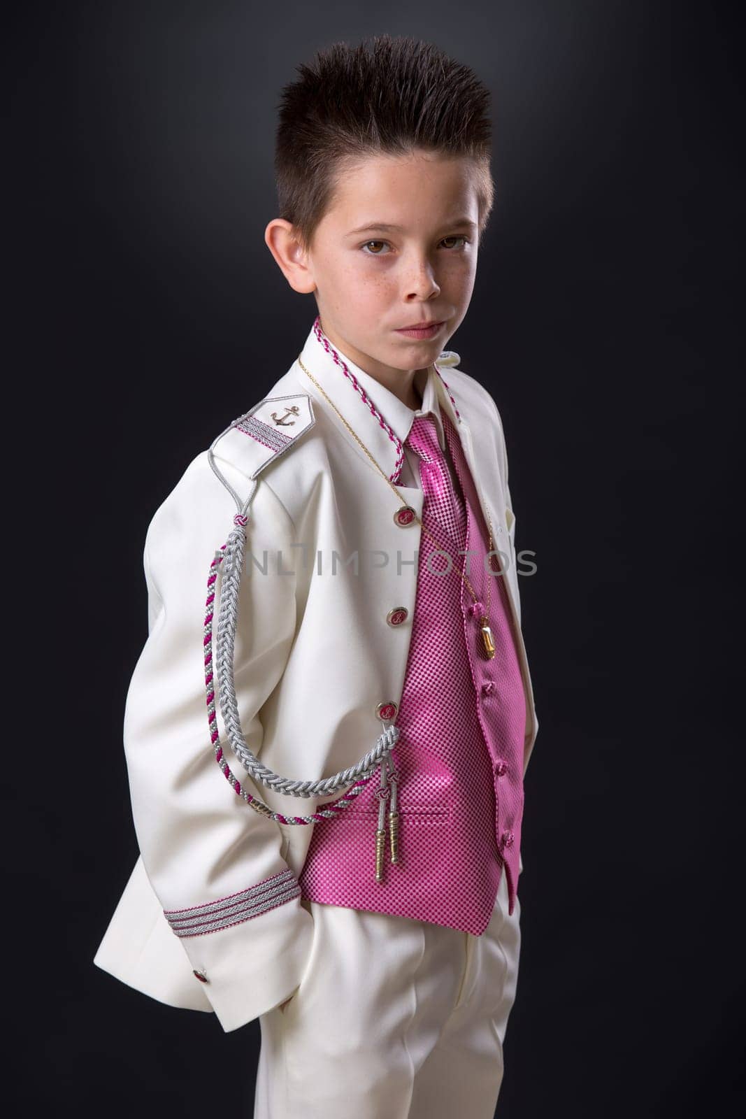 Young boy standing in his First Holy Communion looking at camera seriously on a black background.