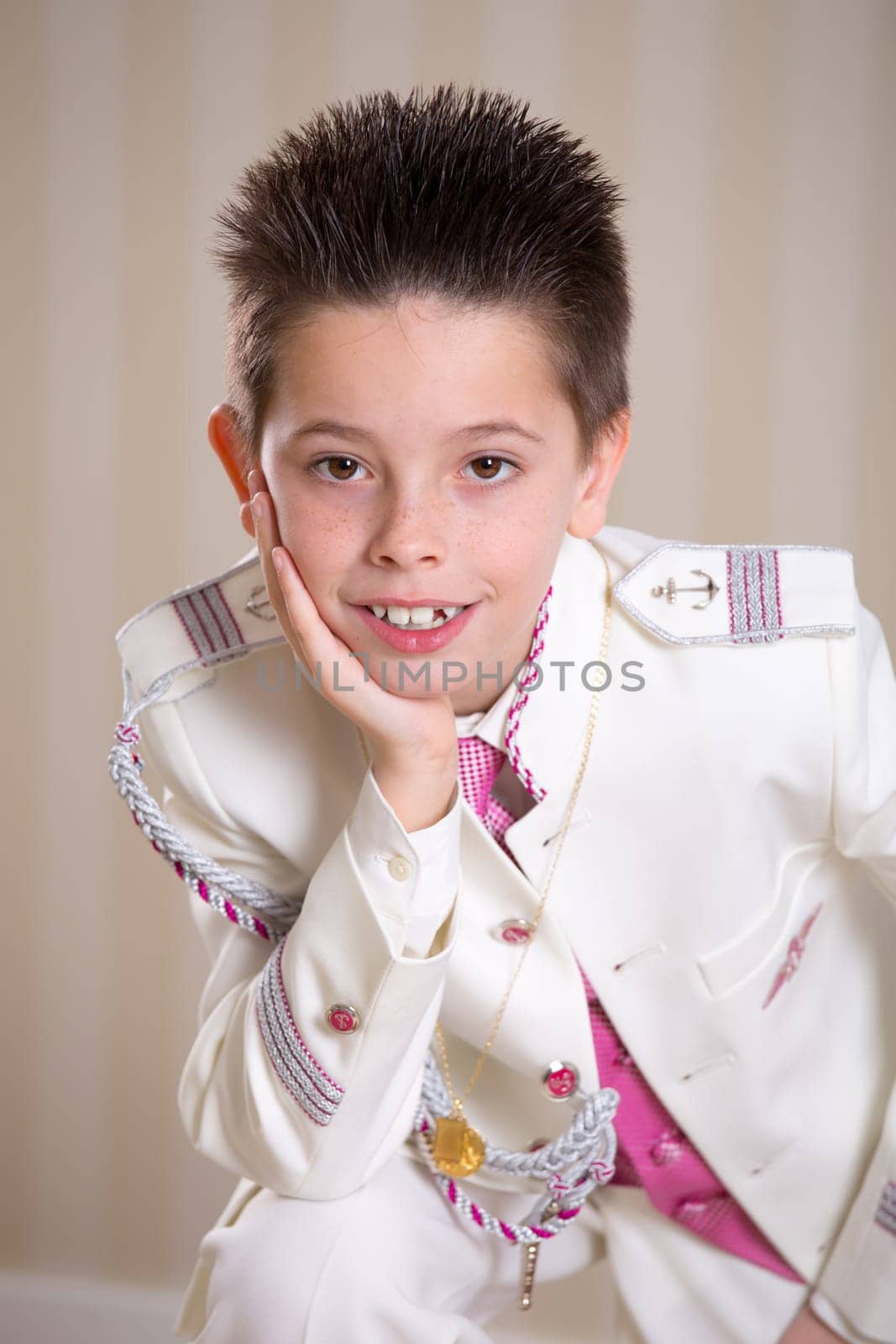 Young boy resting his head on his hand and looking at camera celebrating his First Holy Communion