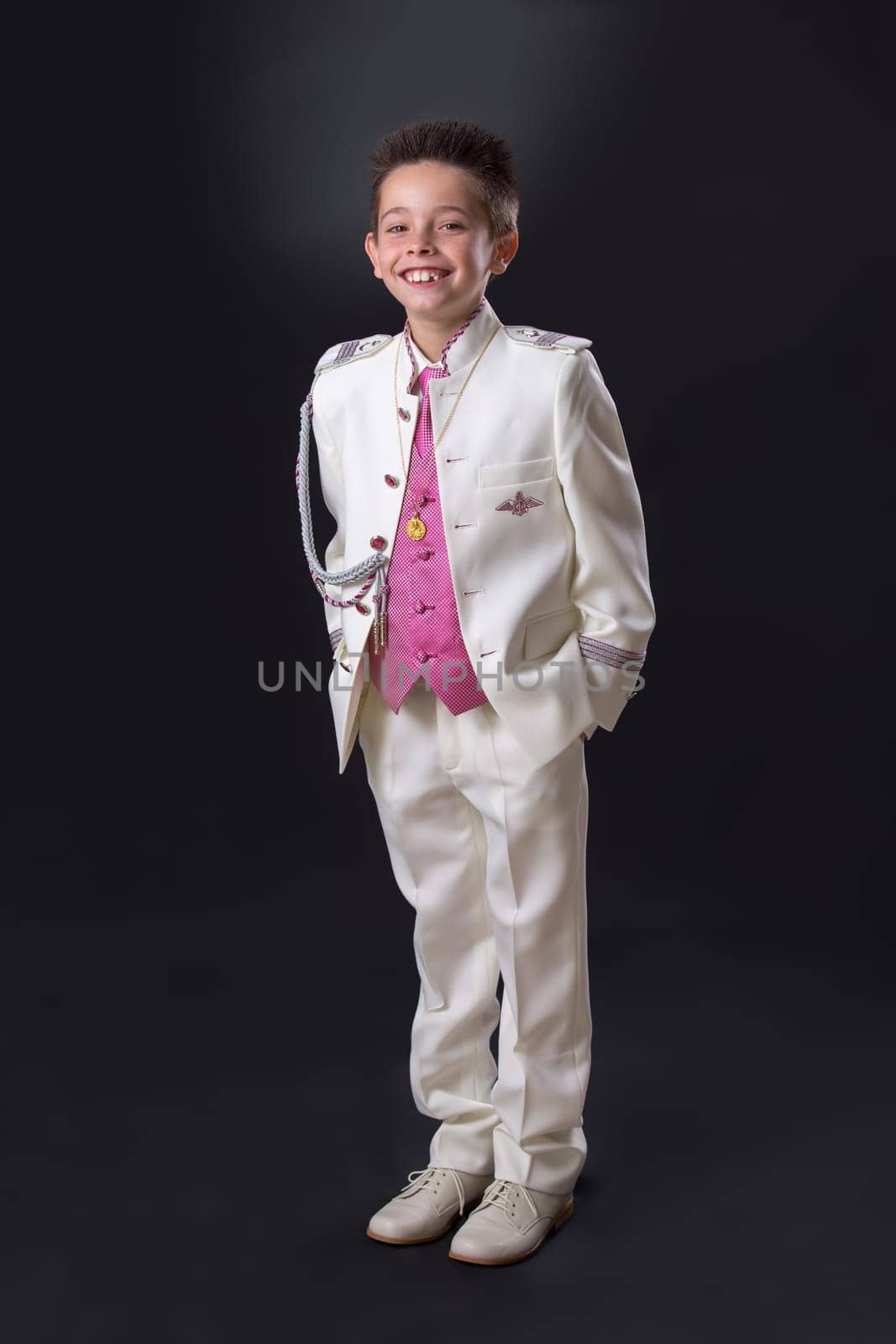 Young boy celebrating his First Holy Communion looking at camera and standing on a black background.