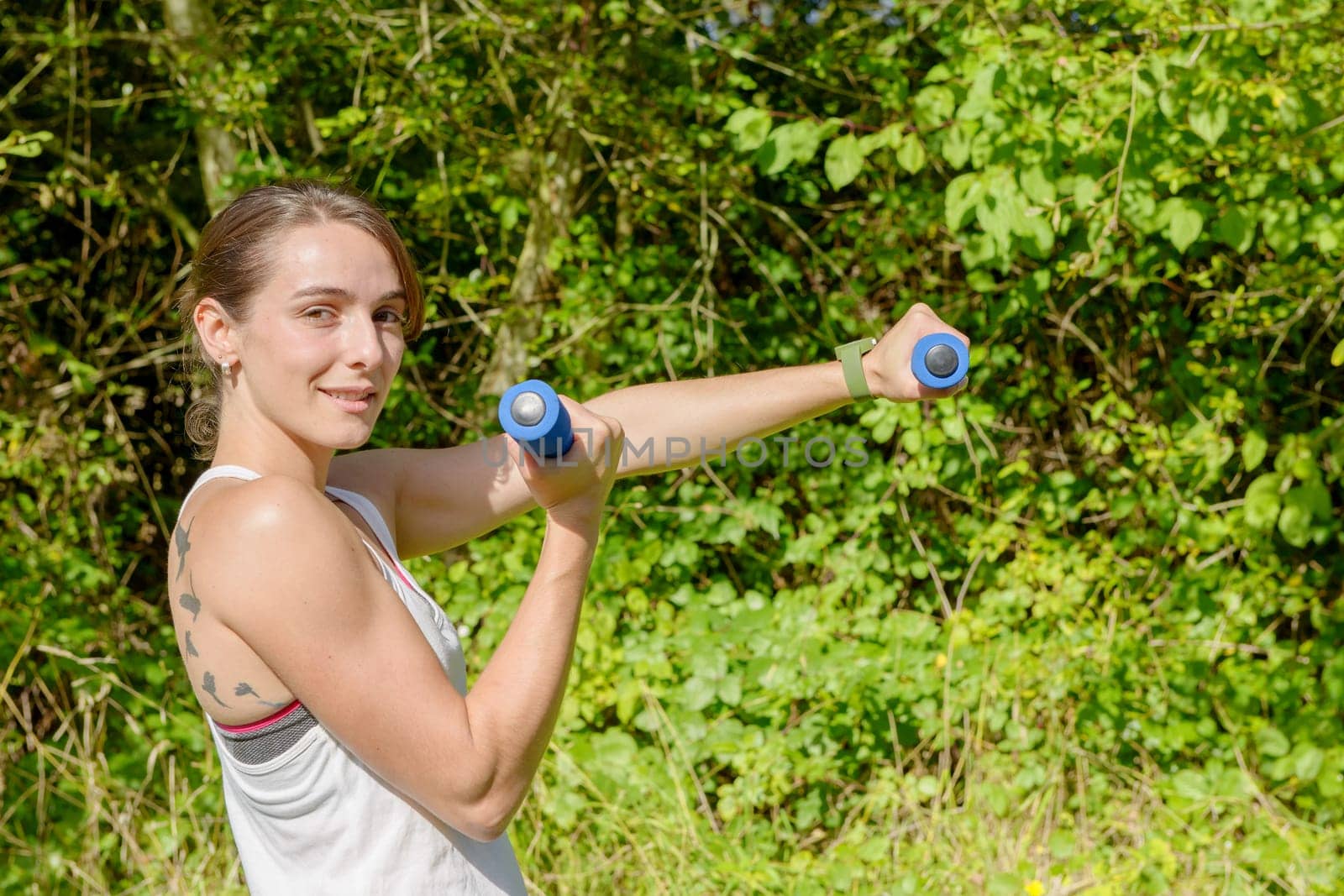 Fitness woman doing exercises with blue dumbbells in the countryside