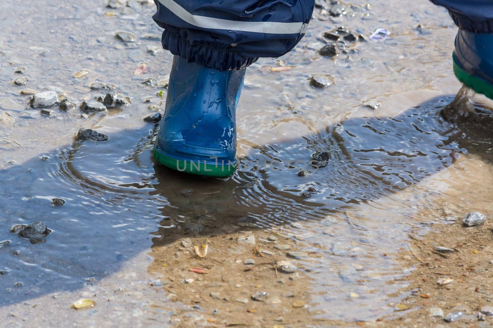 Child with blue rubber boots in a puddle. Close-up..