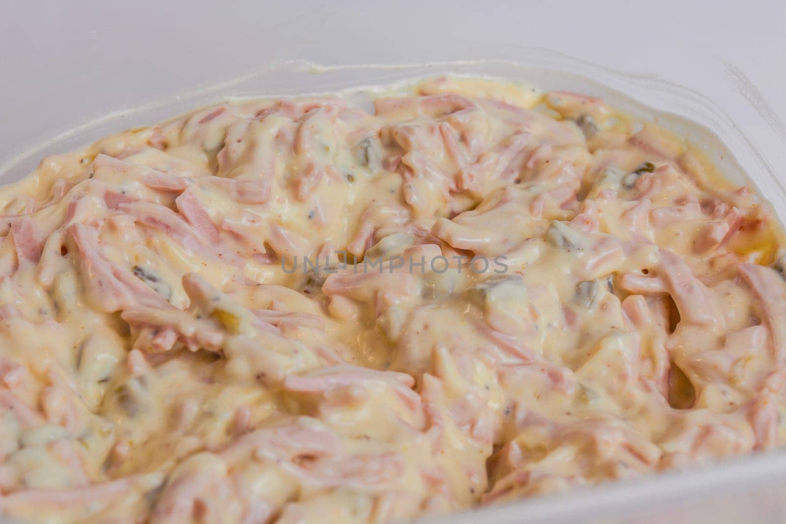 A small bowl of meat salad with mayonnaise on a white plate..