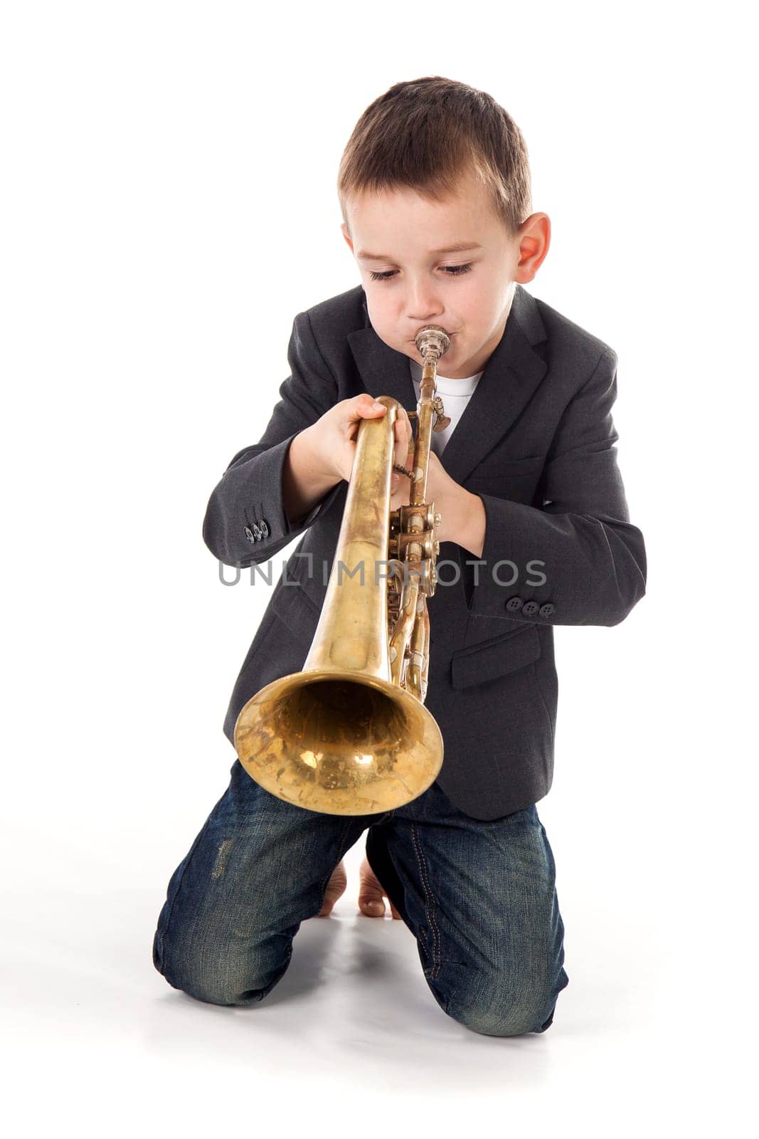 young boy blowing into a trumpet against white background