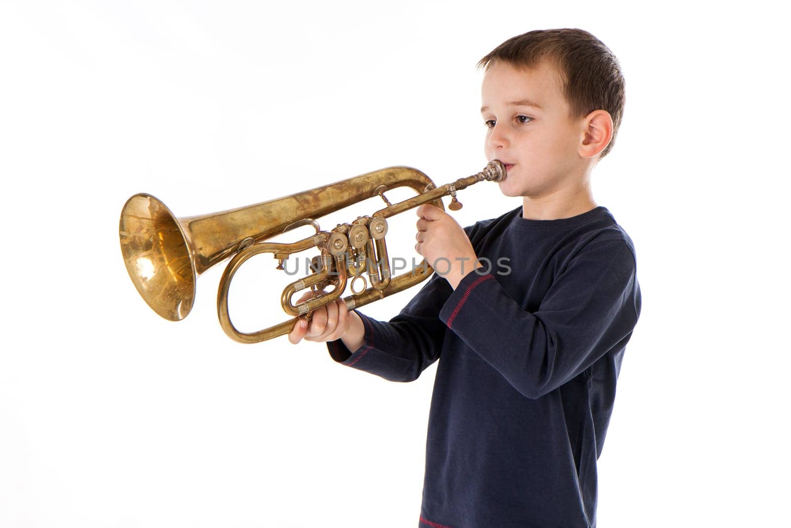 young boy blowing into a trumpet against white background