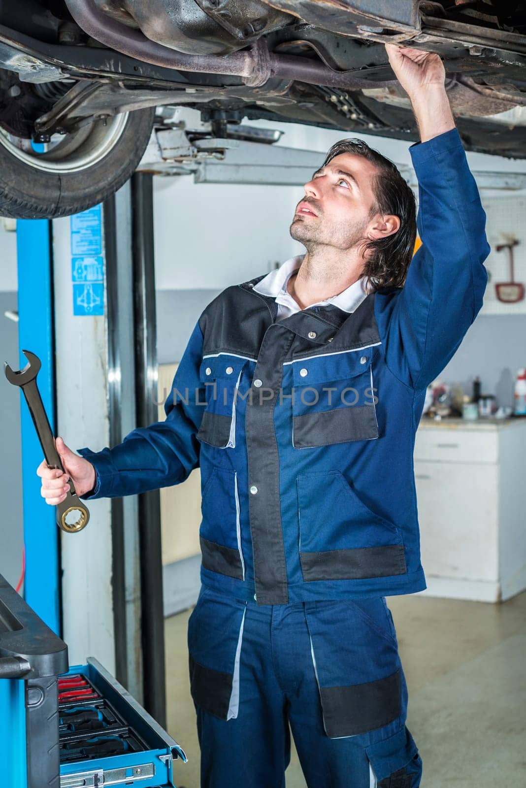 Portrait of a young male mechanic repairing a lifted car with a  big wrench