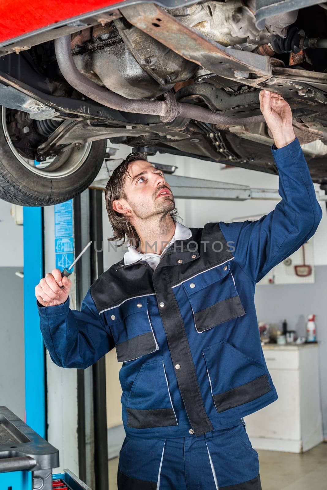 Portrait of a mechanic checking the condition a lifted red car