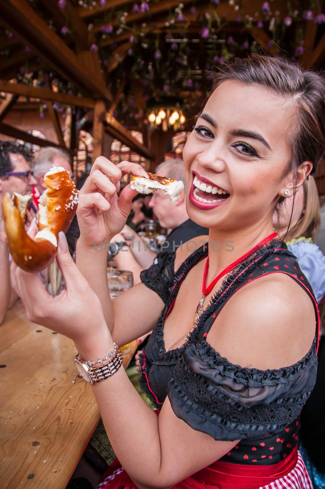 Attractive young woman in traditional Dirndl ot tracht eating Oktoberfest Pretzel, multi-racial Asian, from the Philippines and Caucasian mix