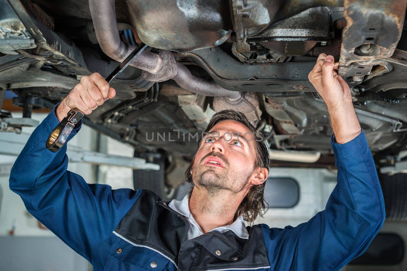 Portrait of a young male mechanic repairing a car, a lifted car