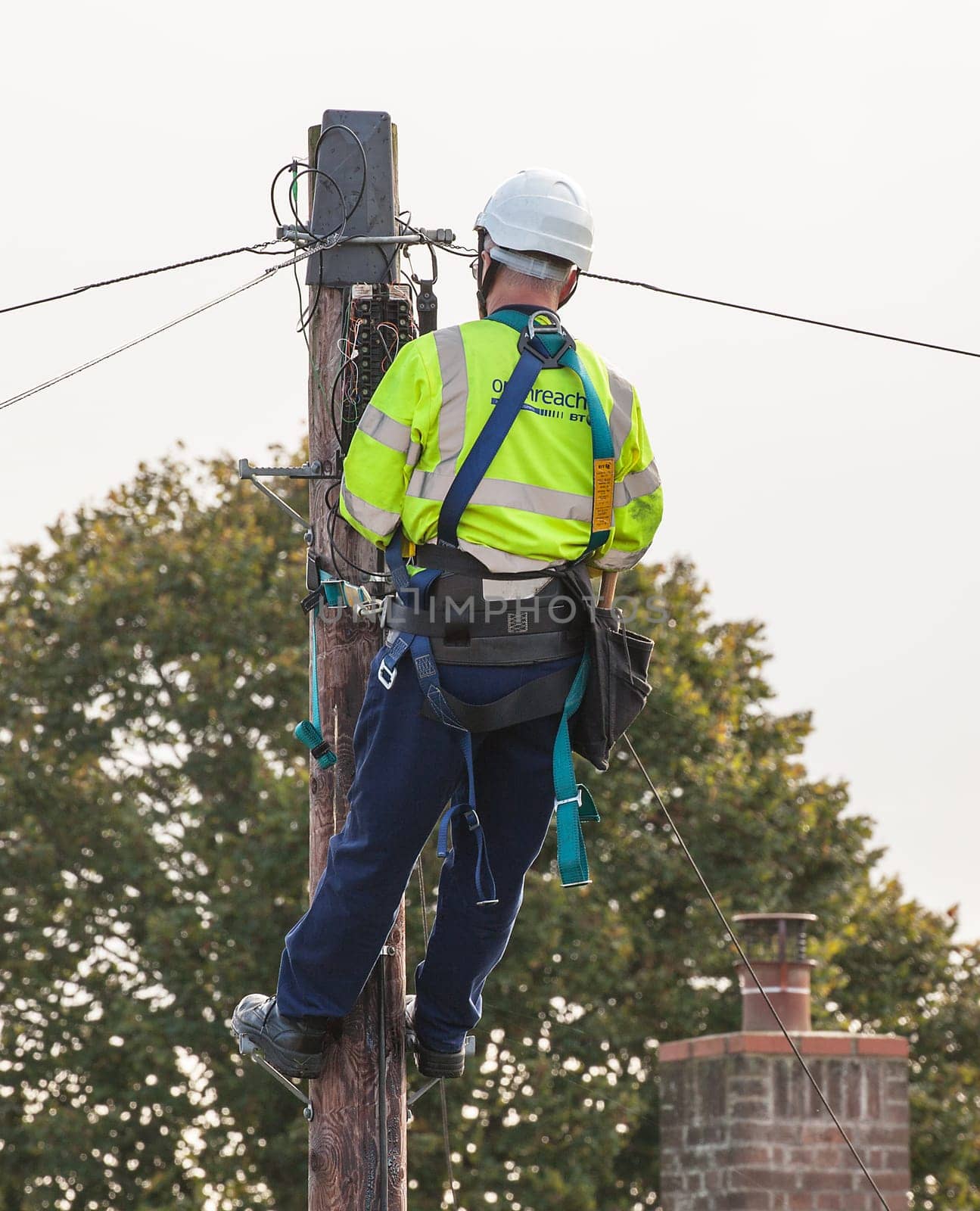 FAKENHAM, NORFOLK / UK - 10th OCTOBER 2016: Openreach BT engineer fixing cables up a pole. UK internet and telephone infrastructure provider at work providing internet and telephone services to rural locations