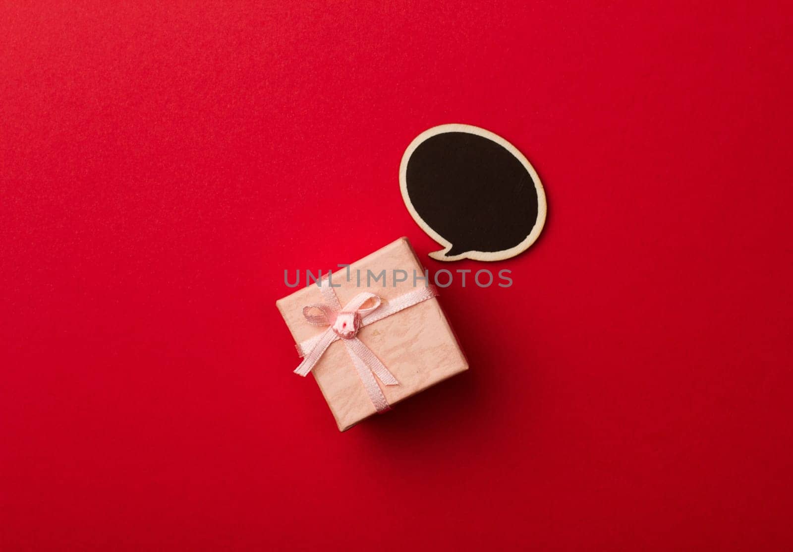 top view of small gift box on red background with wooden black chalk board speech bubble for text
