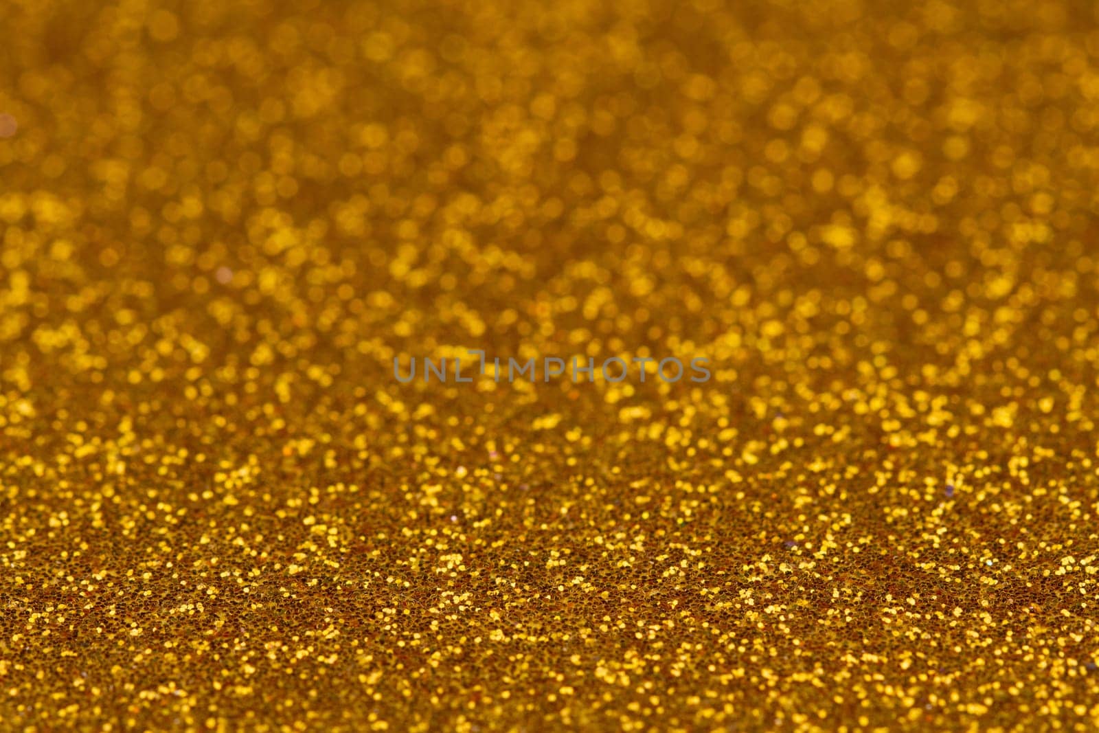 Horizontal glittery gold colored background texture with blurry depth of field