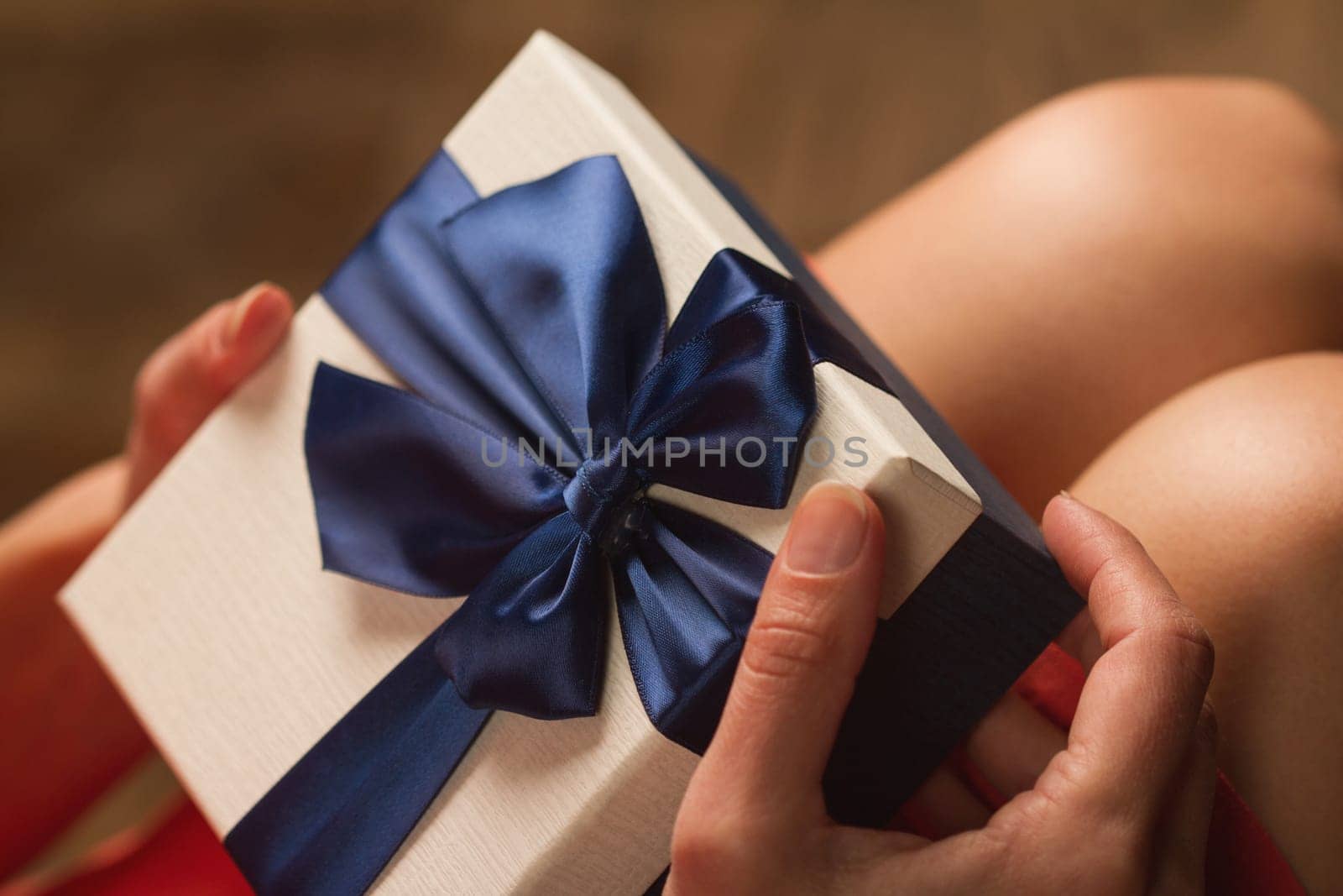 Side view of woman with red dress holding a gift box with blue ribbon on her knees