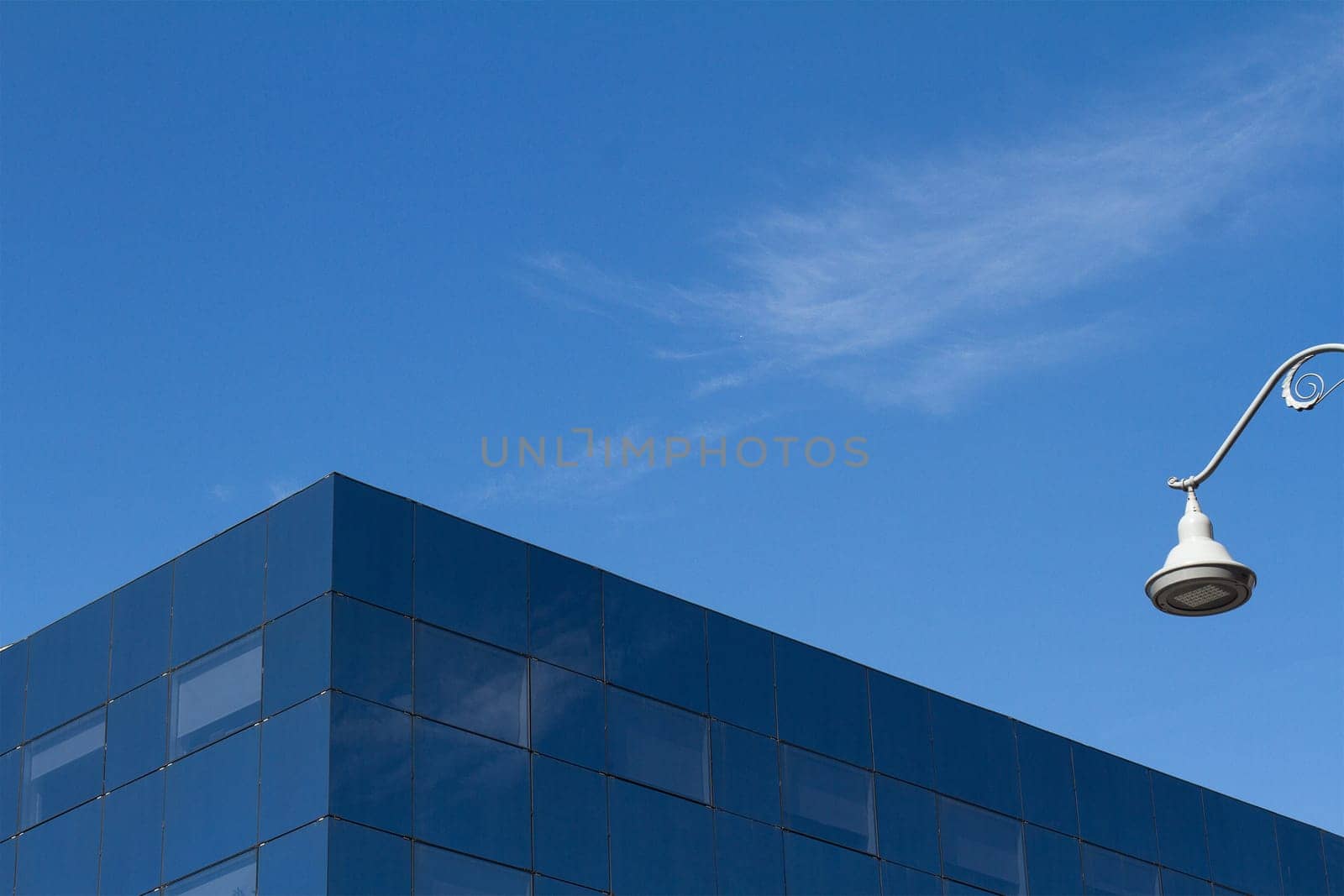 Minimalist photo of a glass office city building detail against a blue sky and a white street light