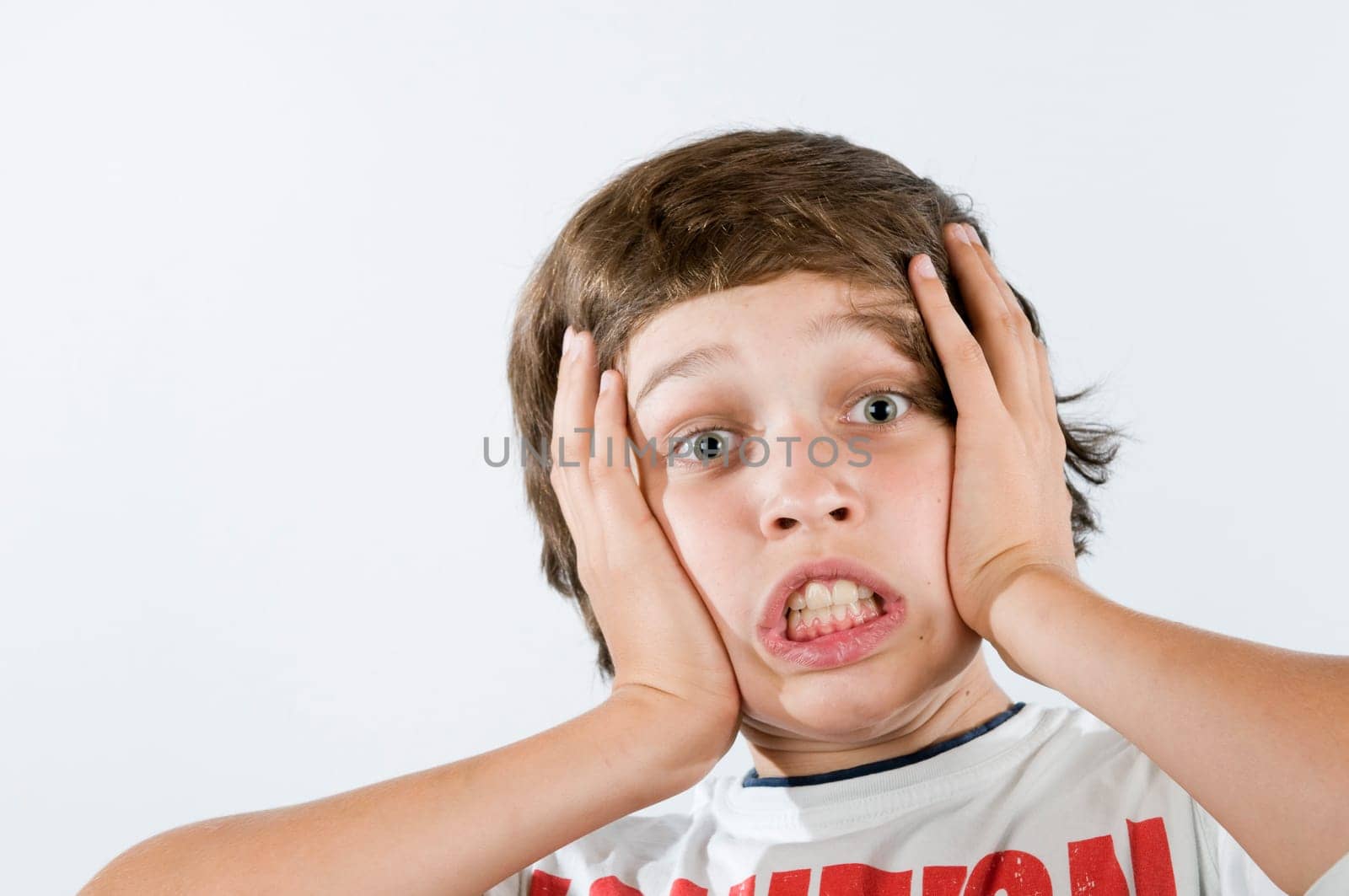 Ten-year-old boy presses his palms on his cheeks with an astonished expression against a white background.