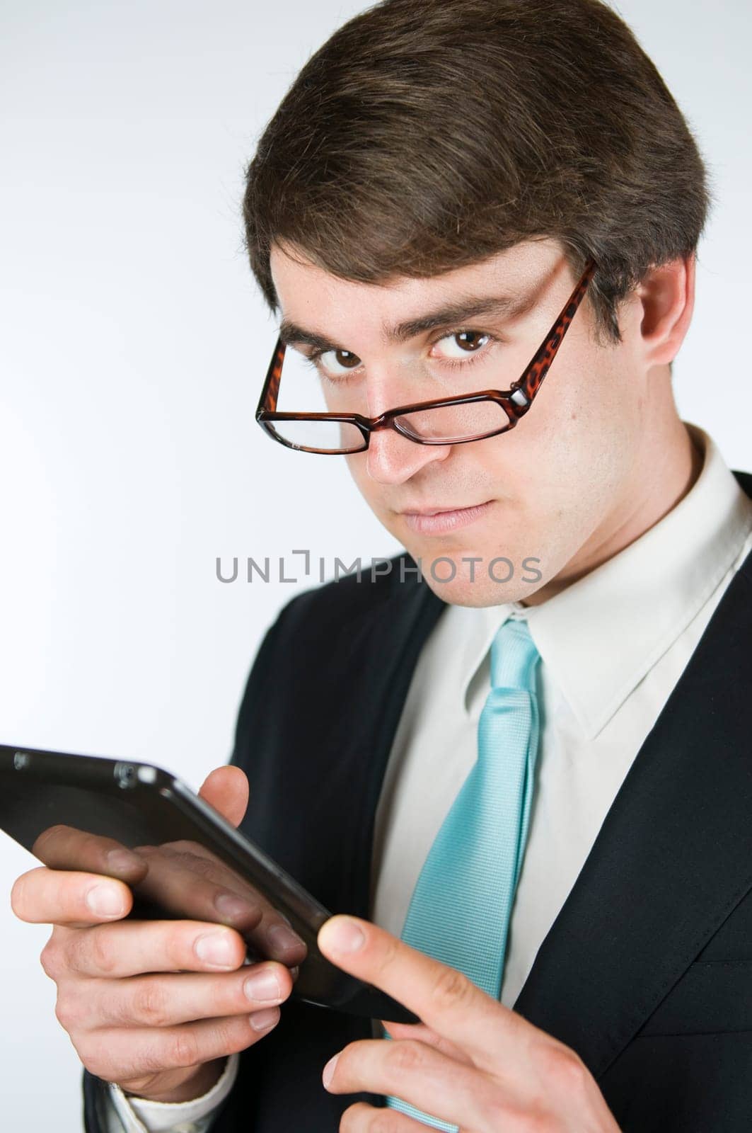 Upper body view of a young man in a suit having a tablet in his hands with a serious look over the edge of the glasses looking towards the camera.