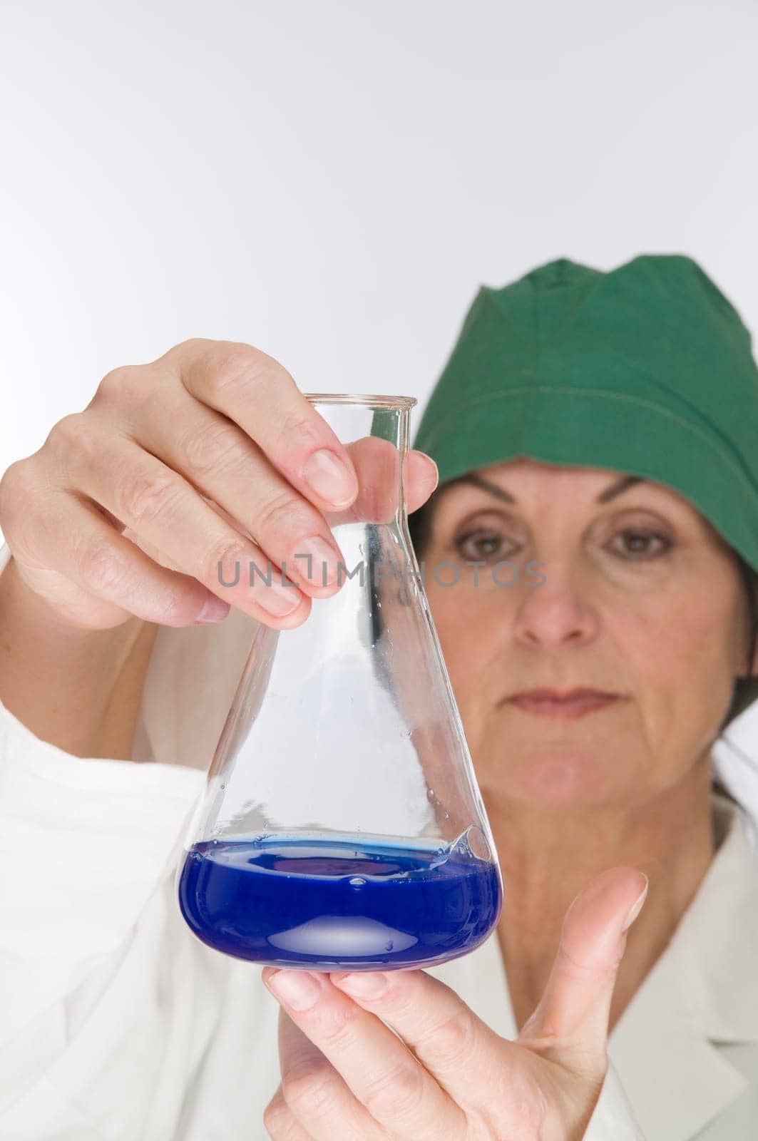 Laboratory technician holds a glass flask with blue liquid and controlling gaze.