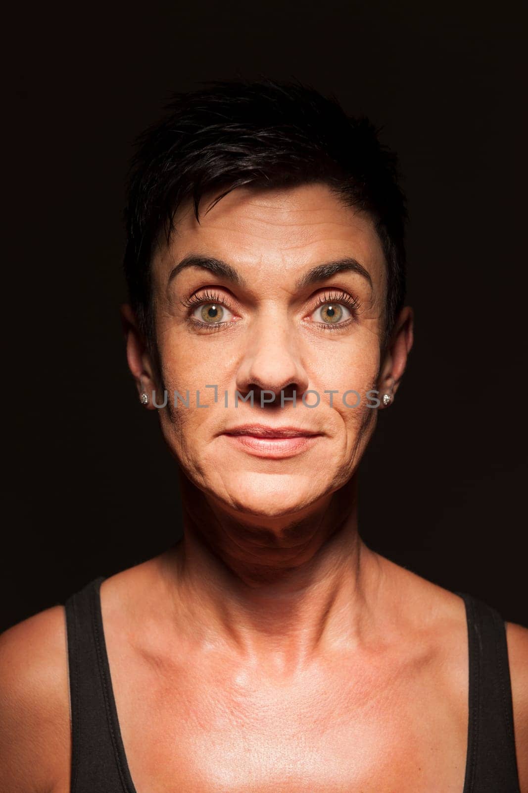 Head-and-shoulder portrait of a middle-aged black-haired woman against a black background looking into the camera in the spotlight.