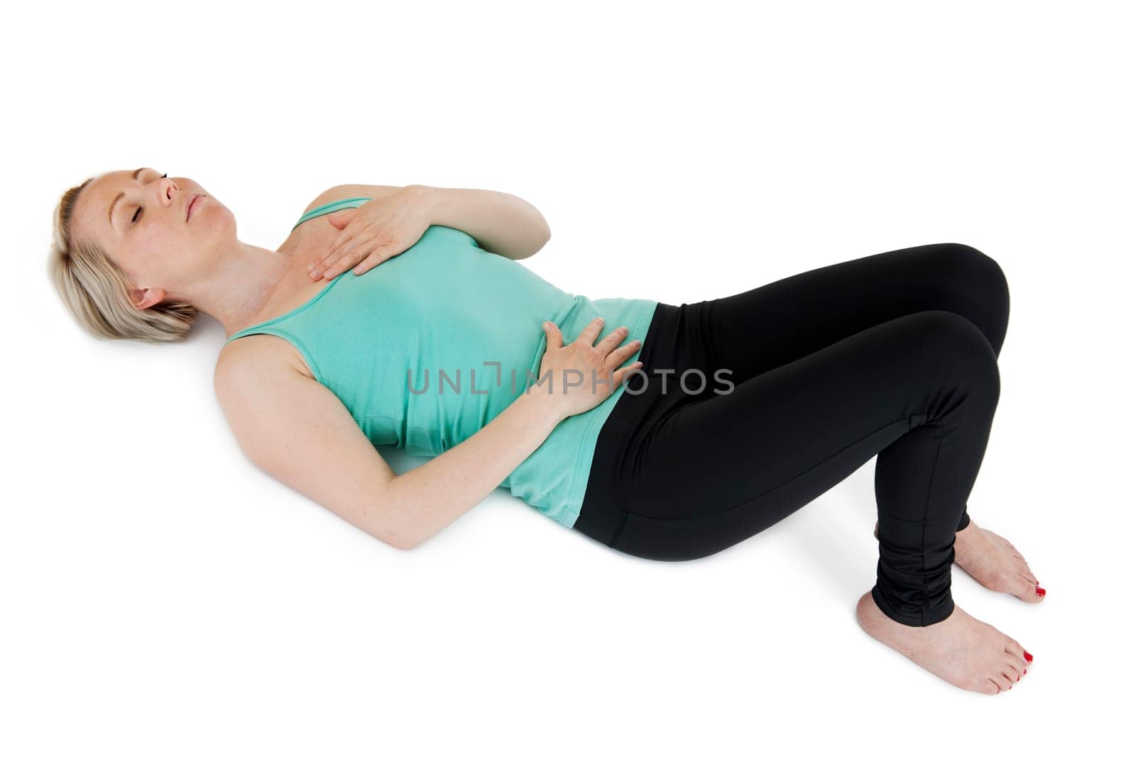 Young woman in supine position on a white background with squatted legs,closed eyes her hands placed on her stomach and chest.