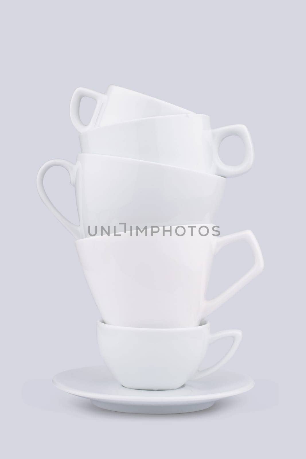 Front view of white ceramic coffee cups piled up on a dish on grey background