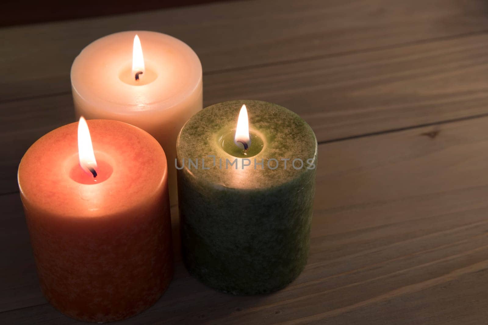 Orange, green and white candles burning on wooden table