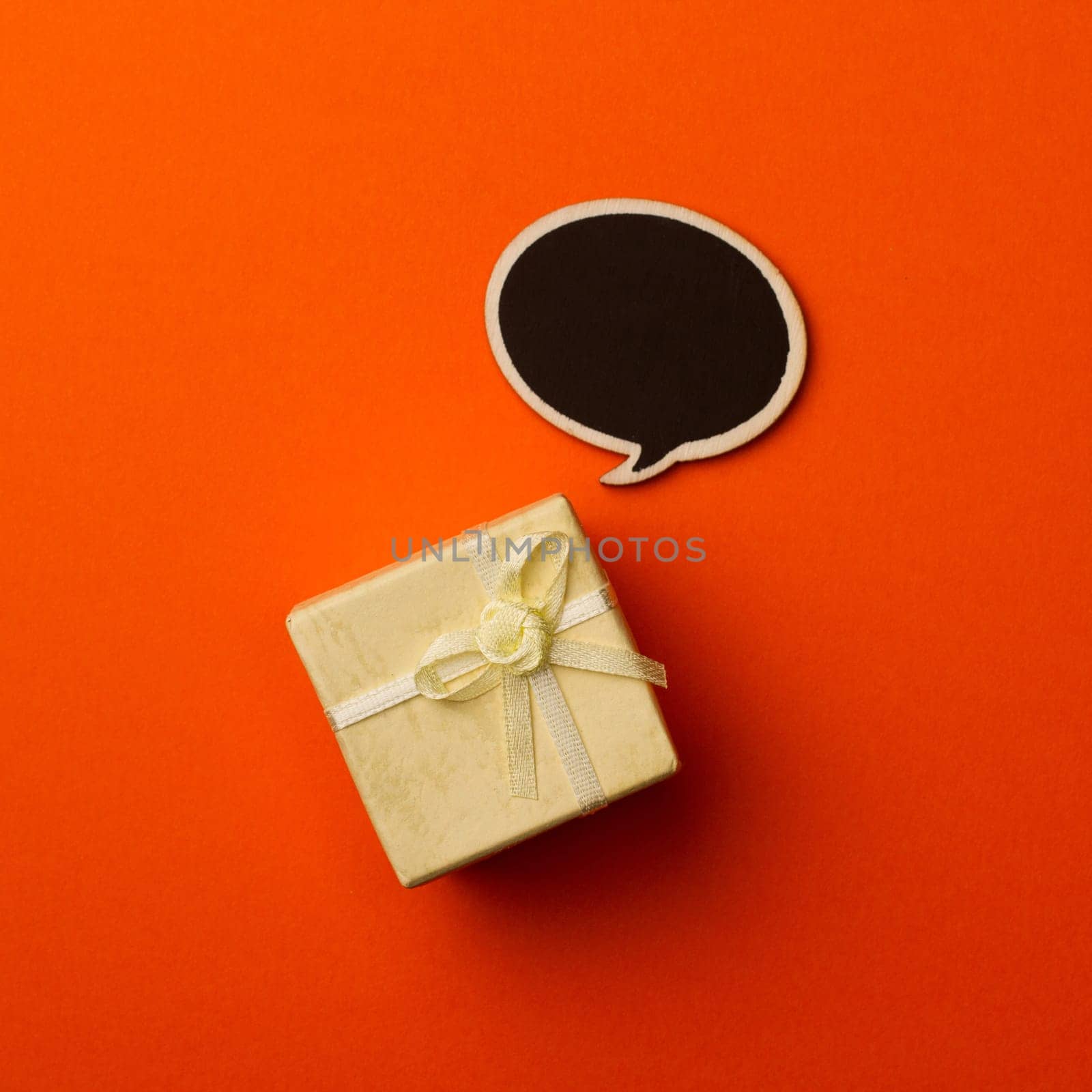 top view of small gift box on orange background with wooden black chalk board speech bubble for text
