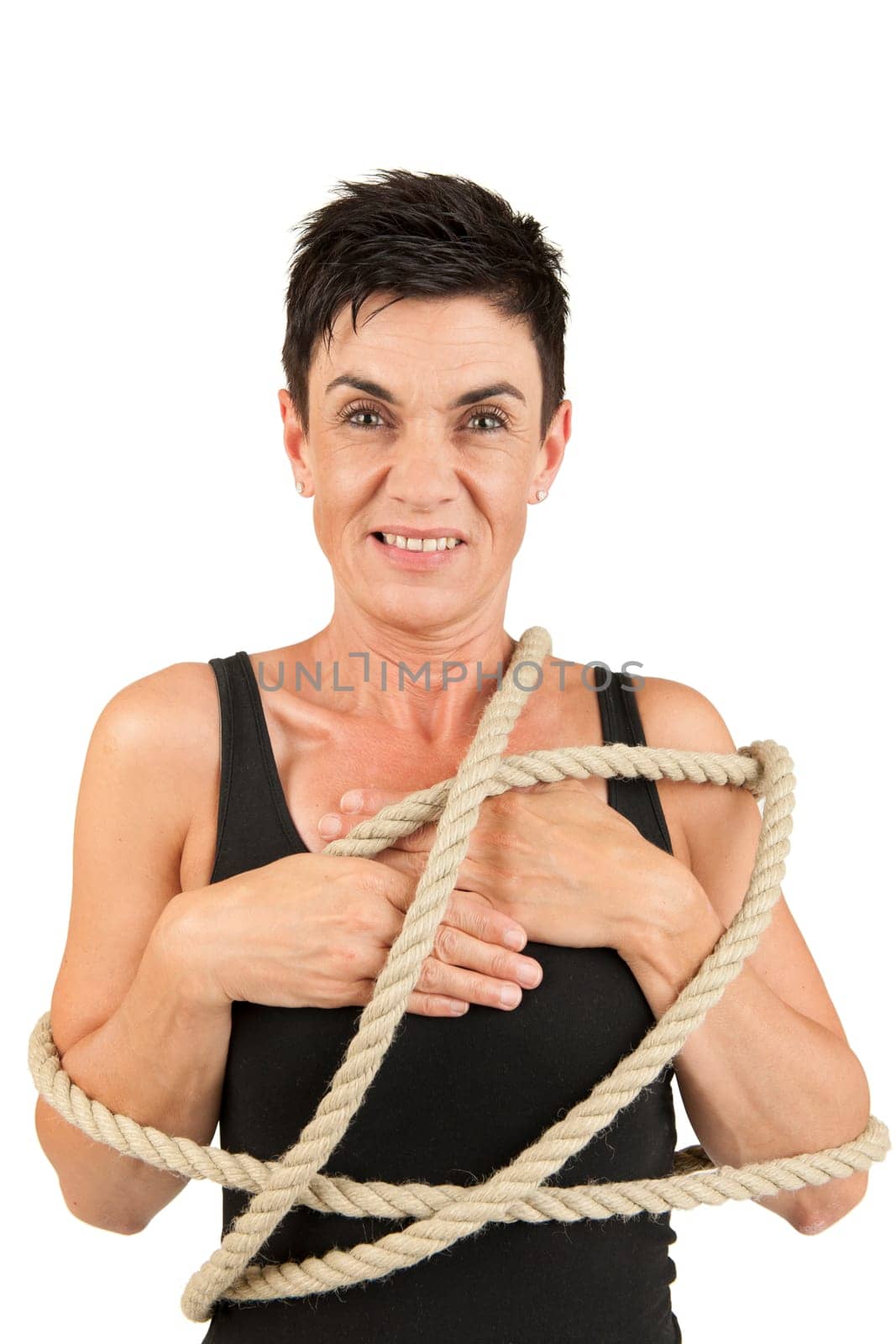 Frontal upper body view of a black-haired middle-aged woman with rope placed around her body against a white background looking dissatisfied into the camera.