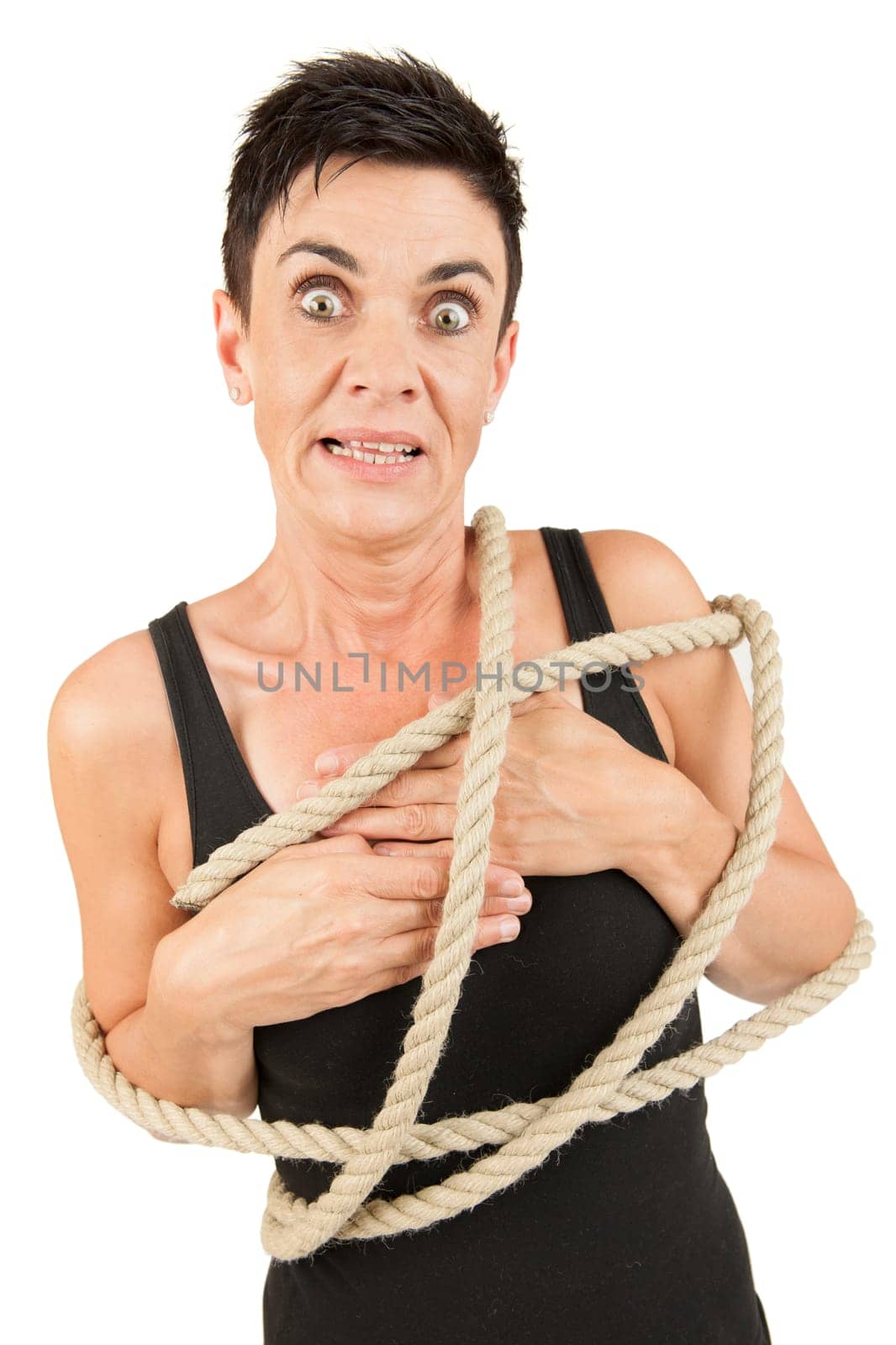 Frontal upper body view of a black-haired middle-aged woman in a black top with rope placed around her body against a white background looking shocked into the camera.