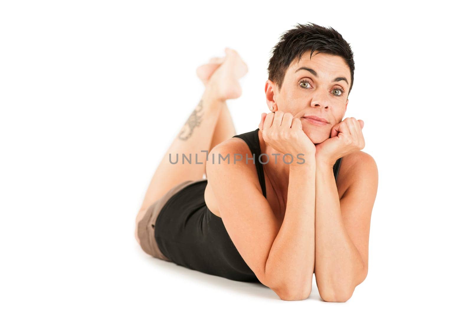 Full-body view of a black-haired middle-aged woman barefoot in shorts and black top lying on her stomach against a white background looking into the camera.