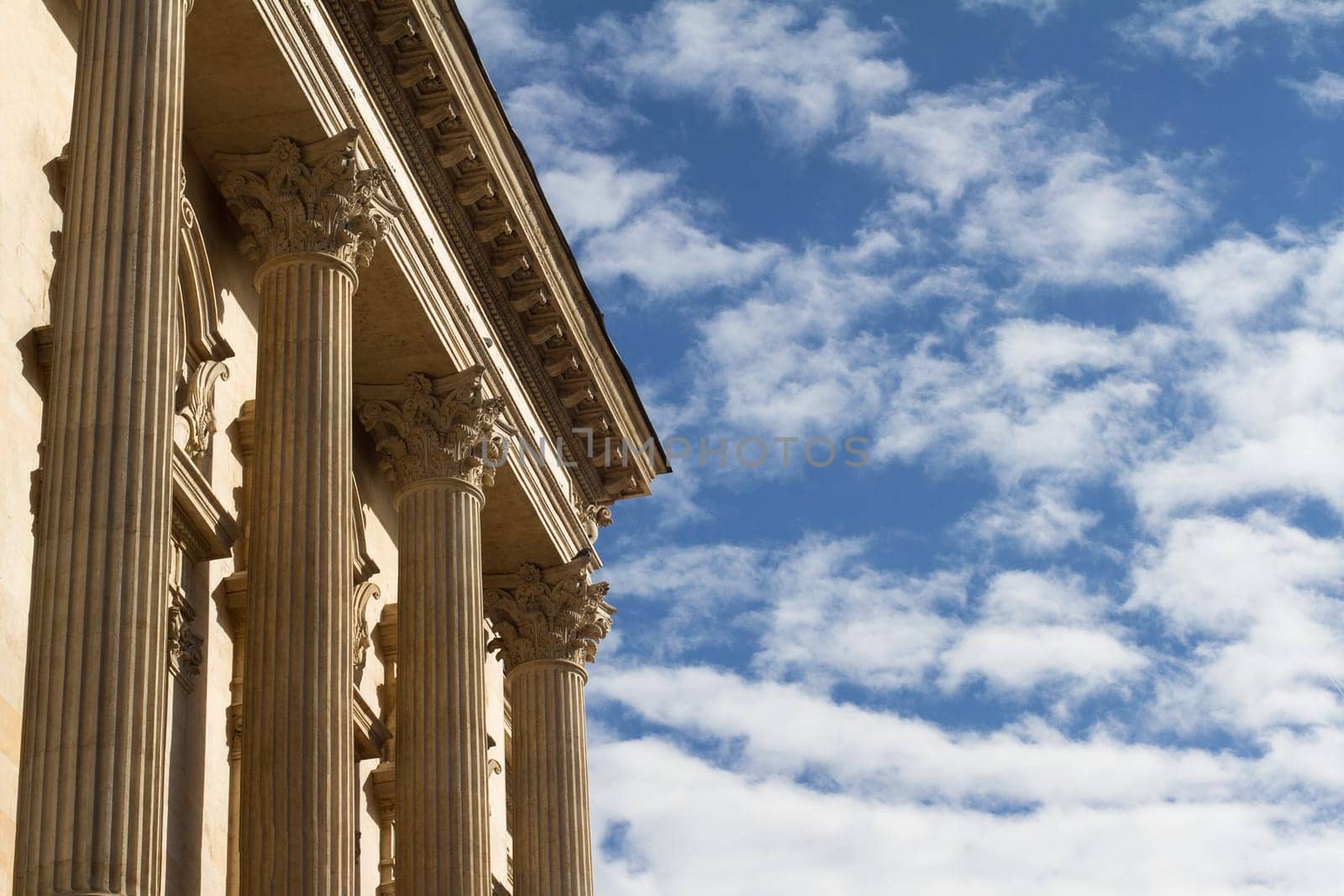 Horizontal photo of classical building columns with blue sky and clouds