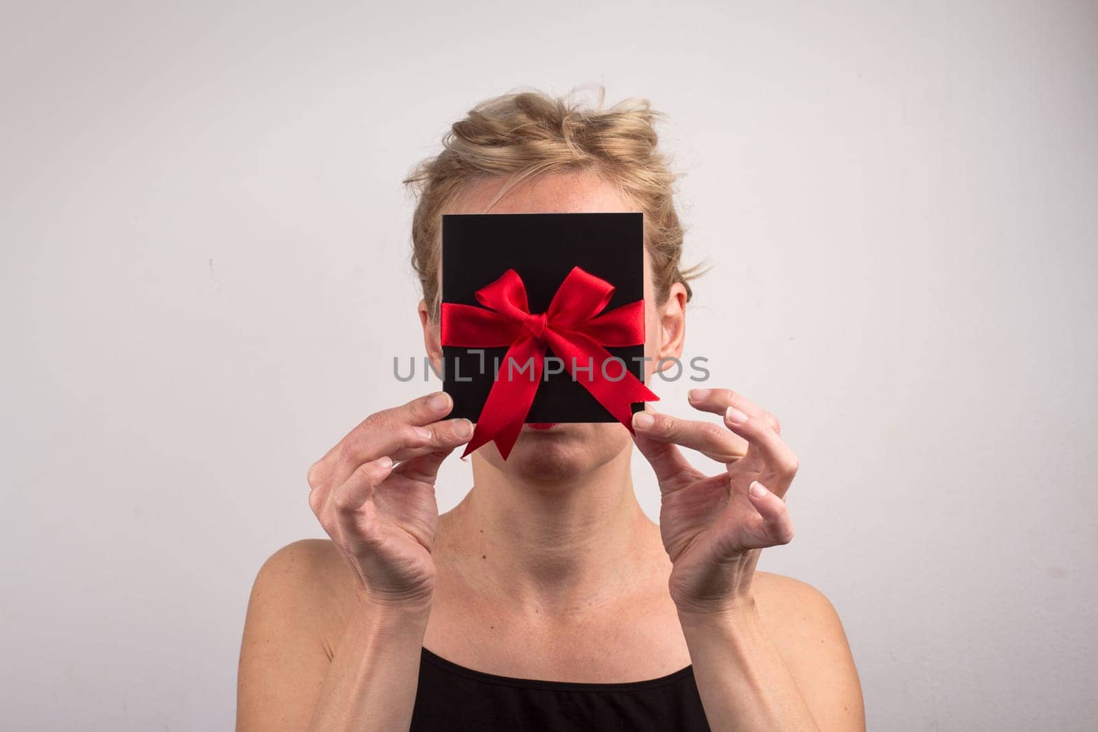 Portrait of a young Caucasian woman holding a black gift card with red ribbon in front of her face