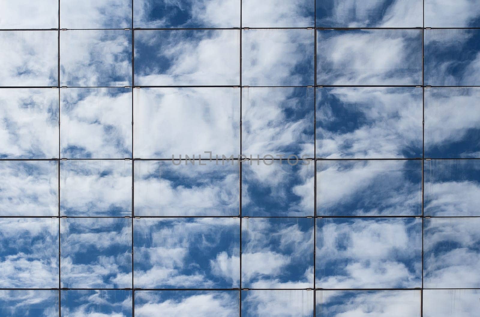 Blue sky and clouds reflected in the windows of tall business office building