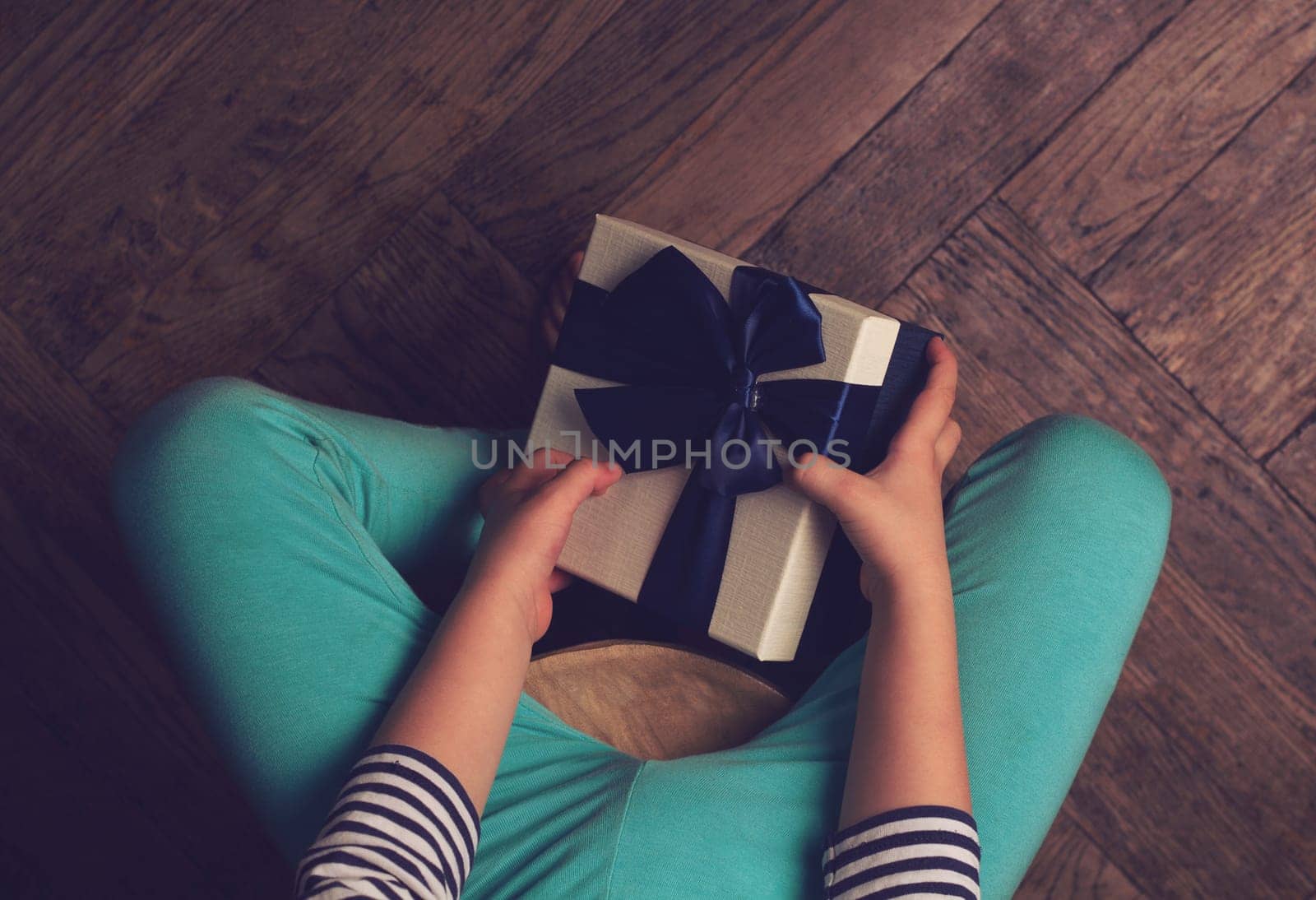 Top view of kid with blue pants and stripes sweater holding a gift box with ribbon in his hands