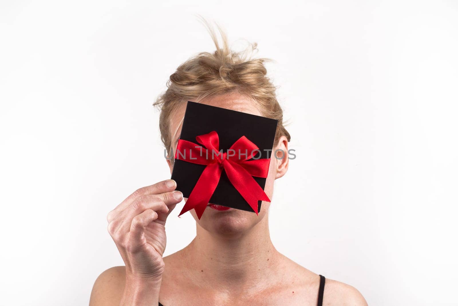 Portrait of a young Caucasian woman holding a black gift card with red ribbon in front of her face