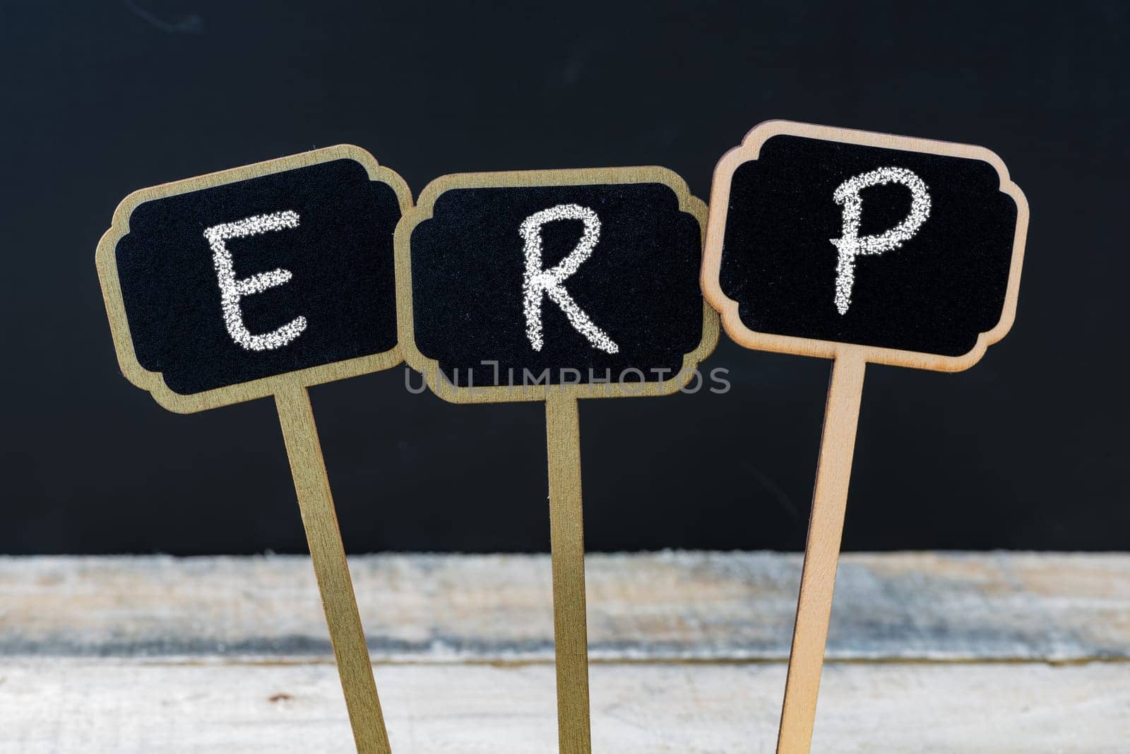 Business acronym ERP as Enterprise Resource Planning written with chalk on wooden mini blackboard labels, defocused chalkboard and wood table in background