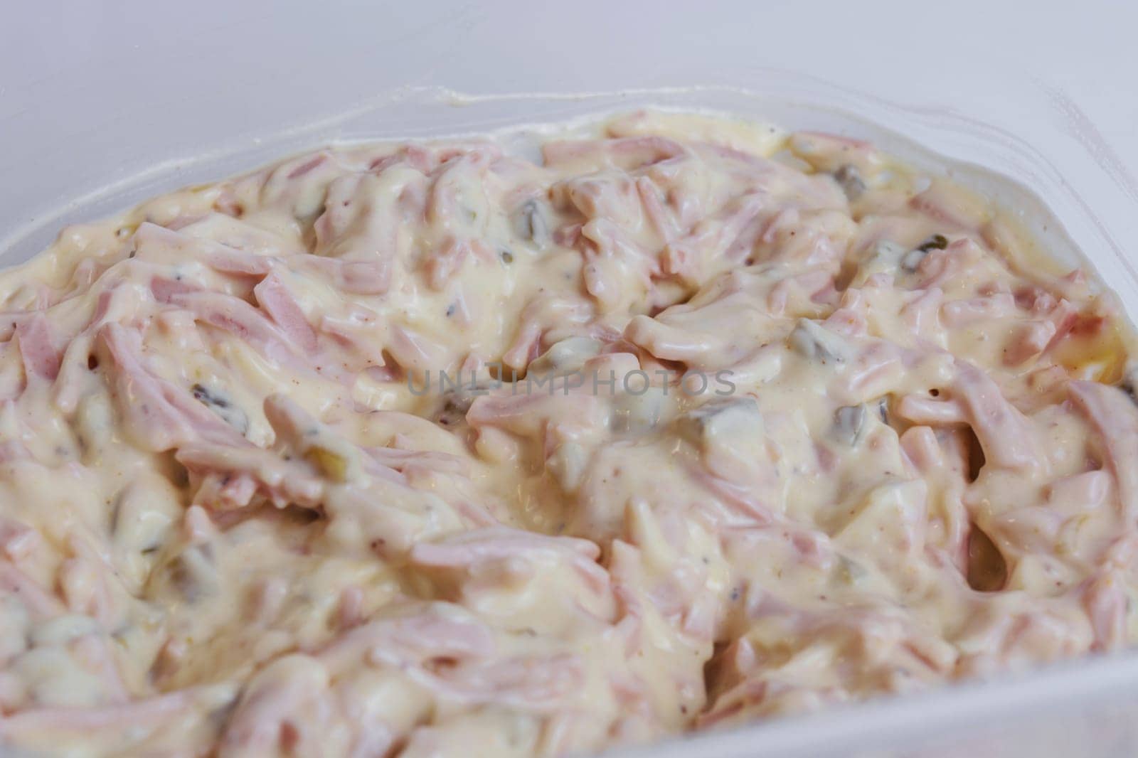 A small bowl of meat salad with mayonnaise on a white plate..