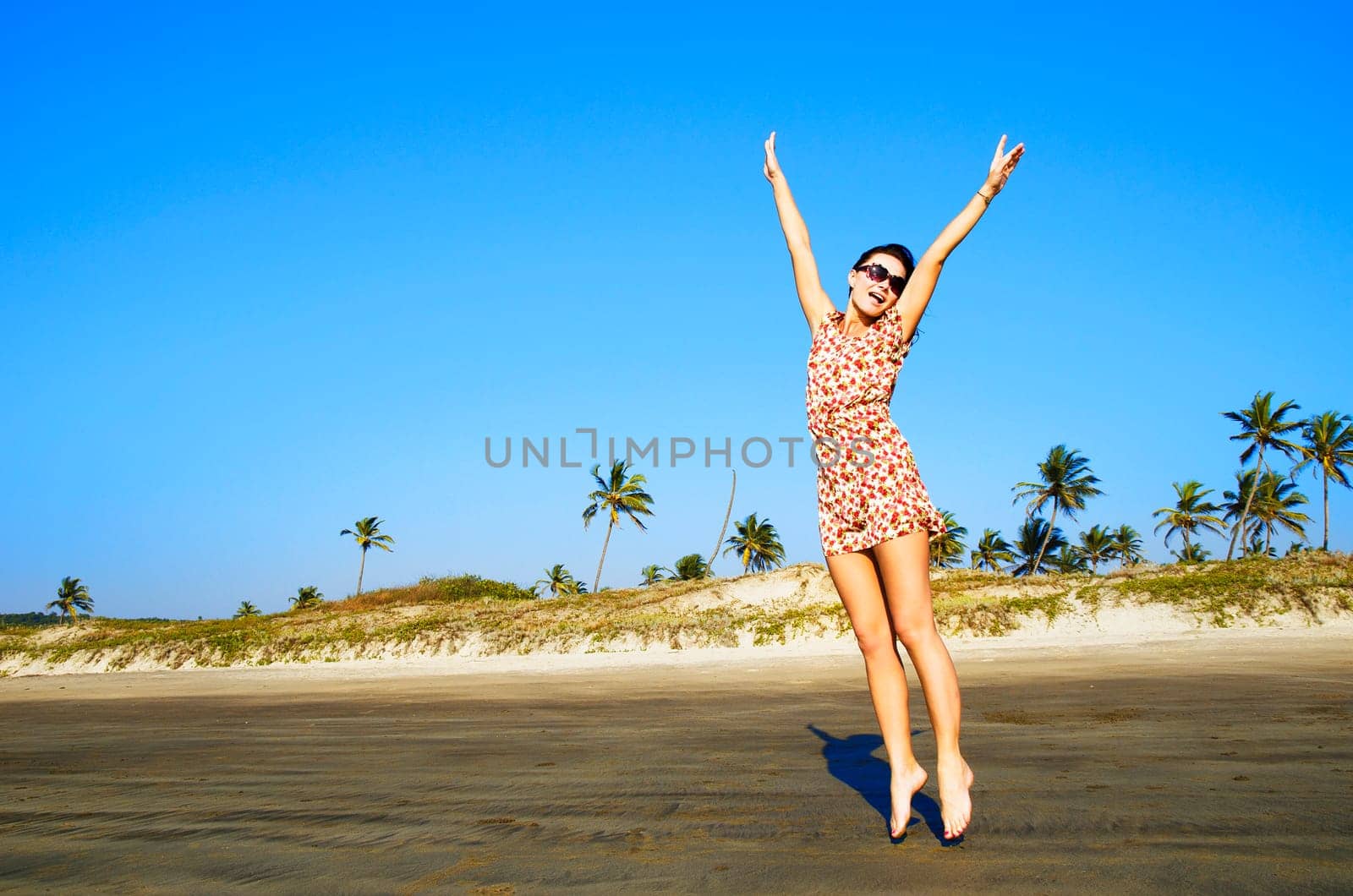 Woman jumping on the sand of the beach with the palms in the background