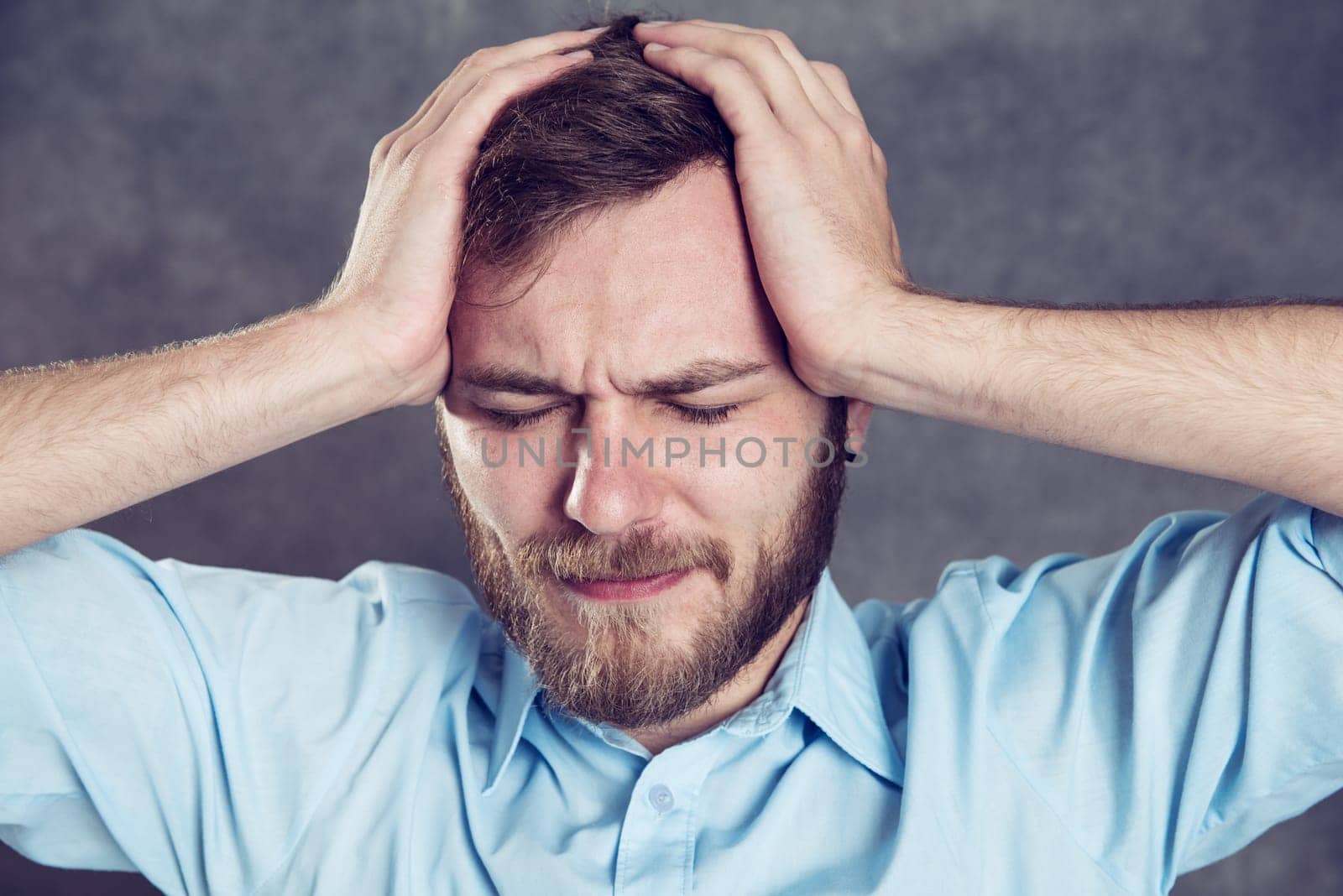 young bearded man in front of gray background has headache