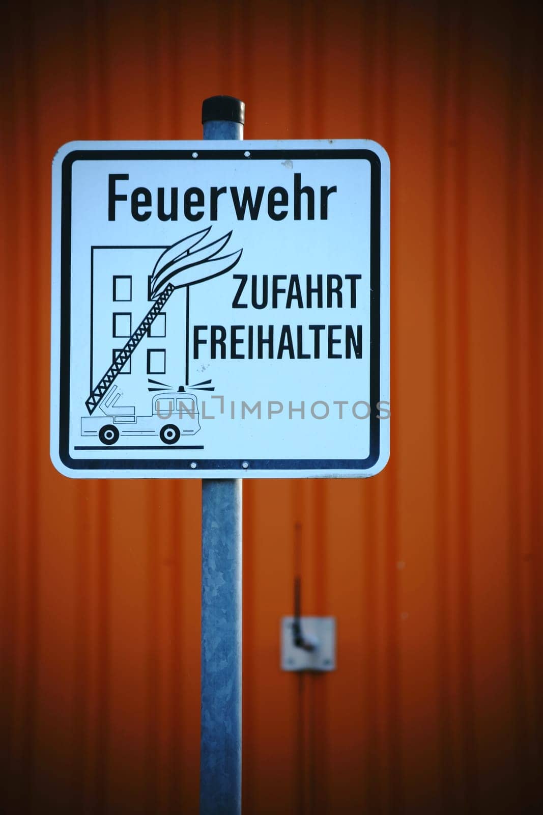 A sign for a fire brigade driveway in front of an abstract orange façade.