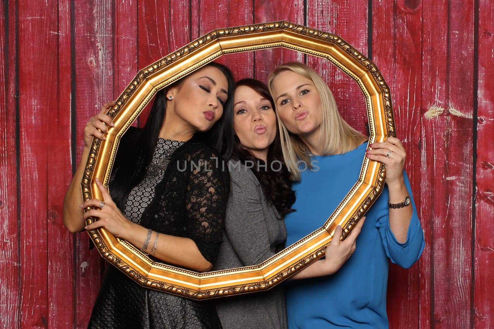Three women look through a picture frame and make a kiss mouth