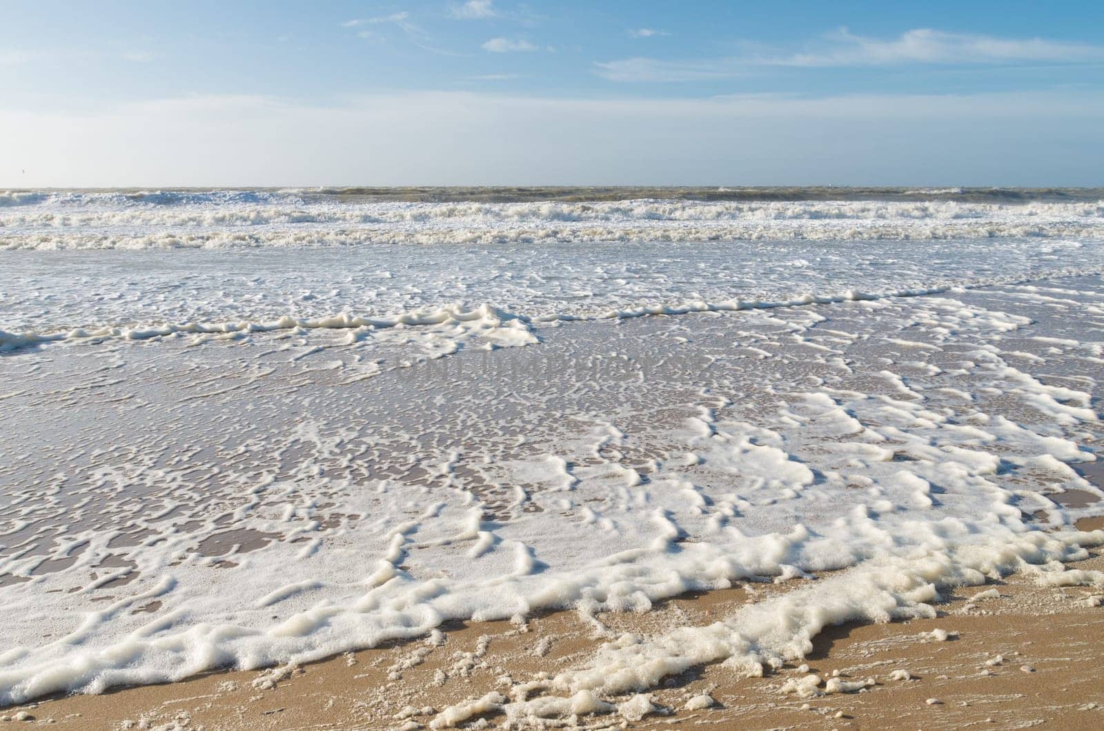 north sea beach full of foam on a windy spring day