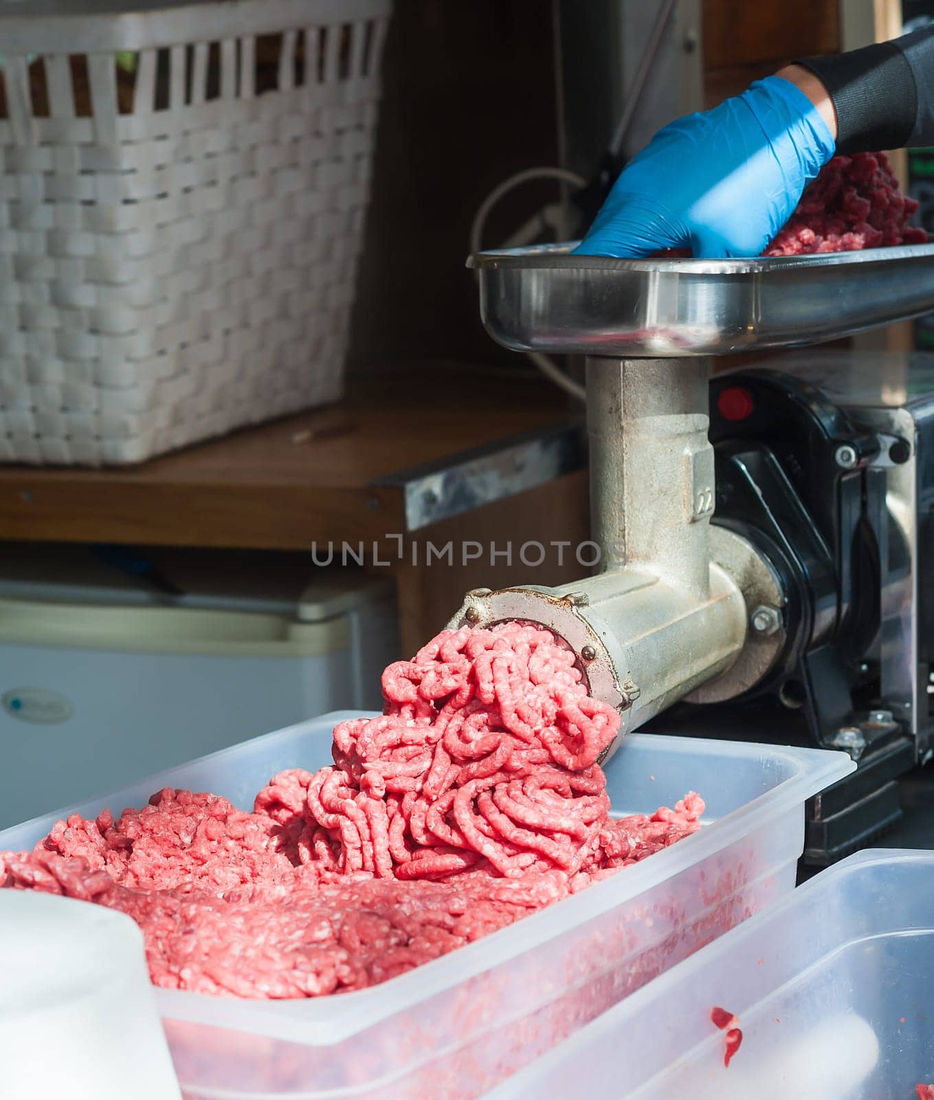 Tray of fresh minced meat. Butcher hand meat grinder and machine that puts the meat back into the machine.