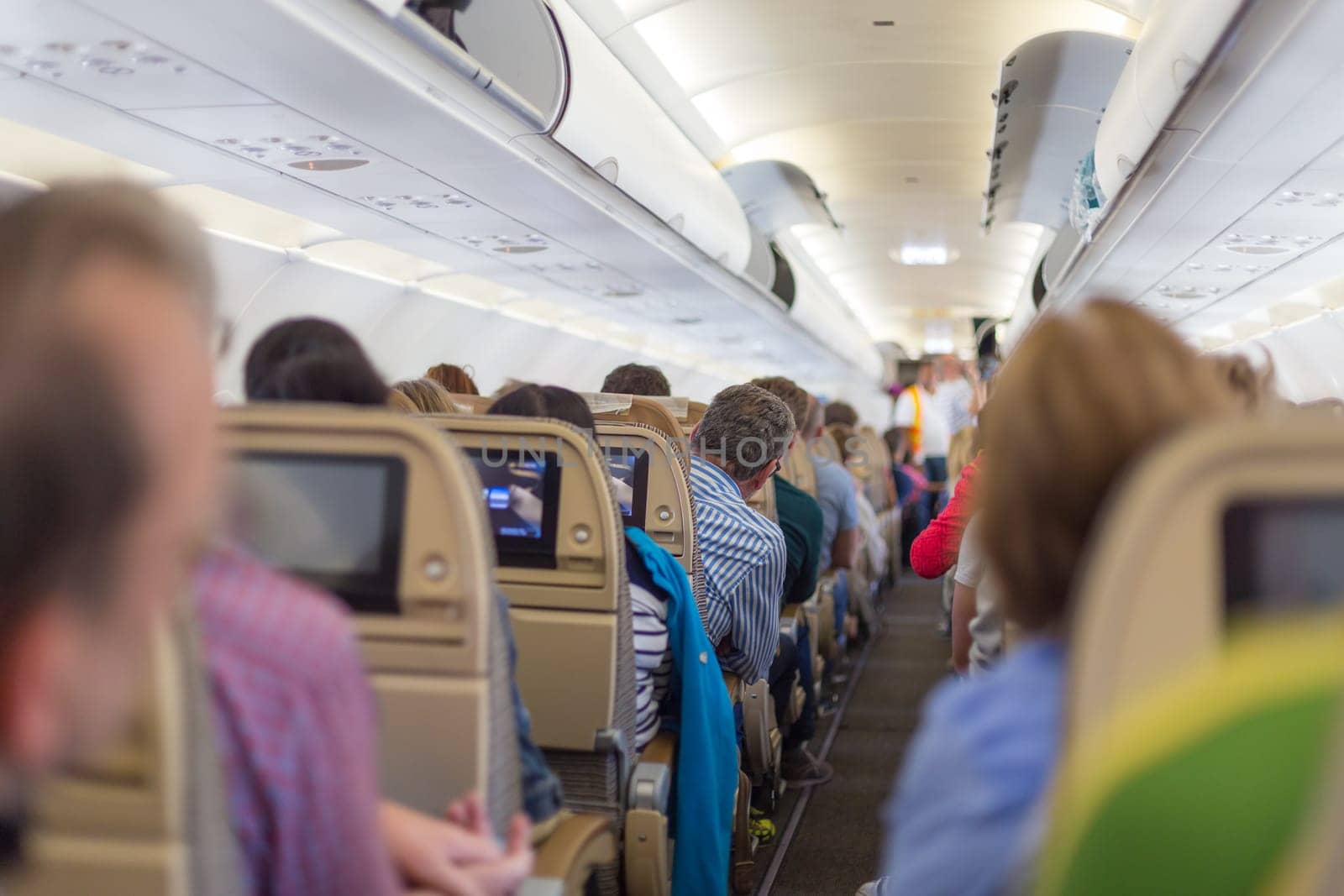 Interior of modern commercial airplane with passengers on their seats waiting to taik off.