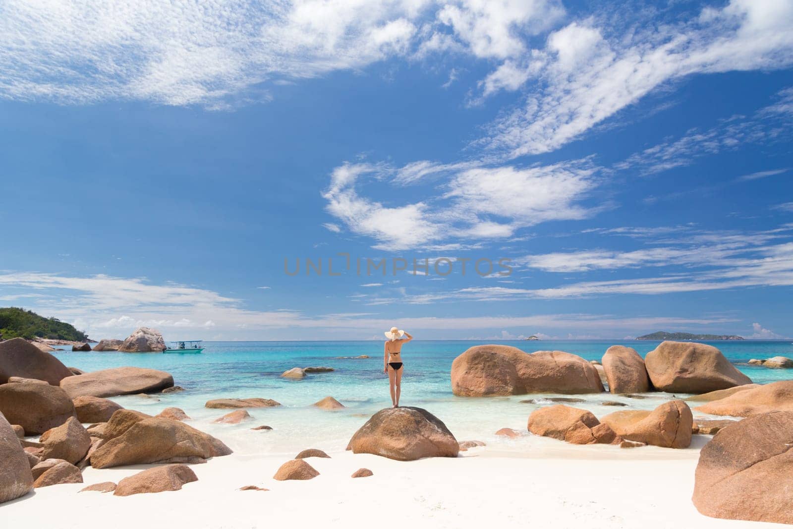Woman wearing black bikini and beach hat, enjoying amazing view on Anse Lazio beach on Praslin Island, Seychelles. Summer vacations on picture perfect tropical beach concept.