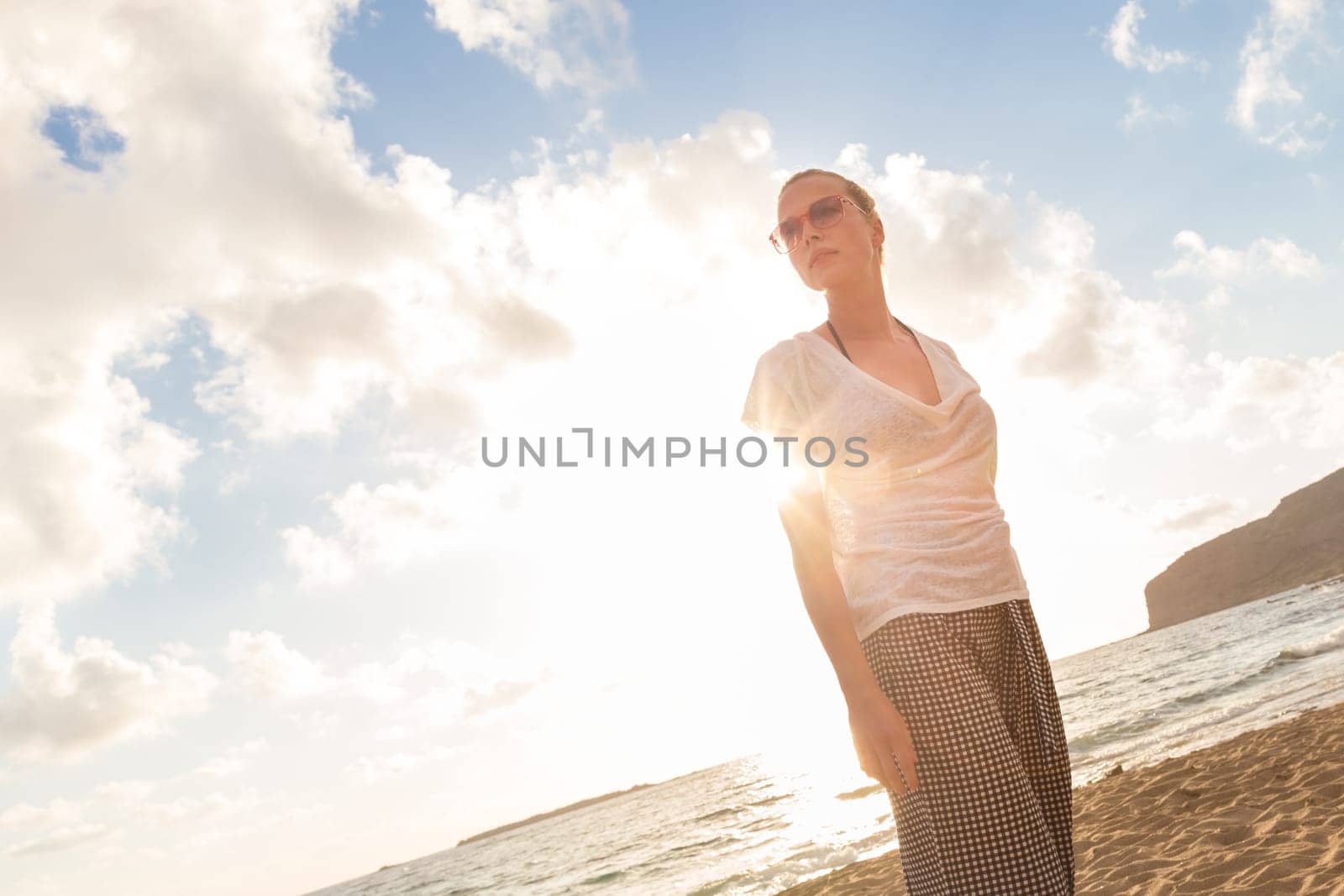 Relaxed woman enjoying sun, freedom and life an a beautiful sandy beach. Young lady feeling free, relaxed and happy. Vacations, freedom, happiness, enjoyment and well being.
