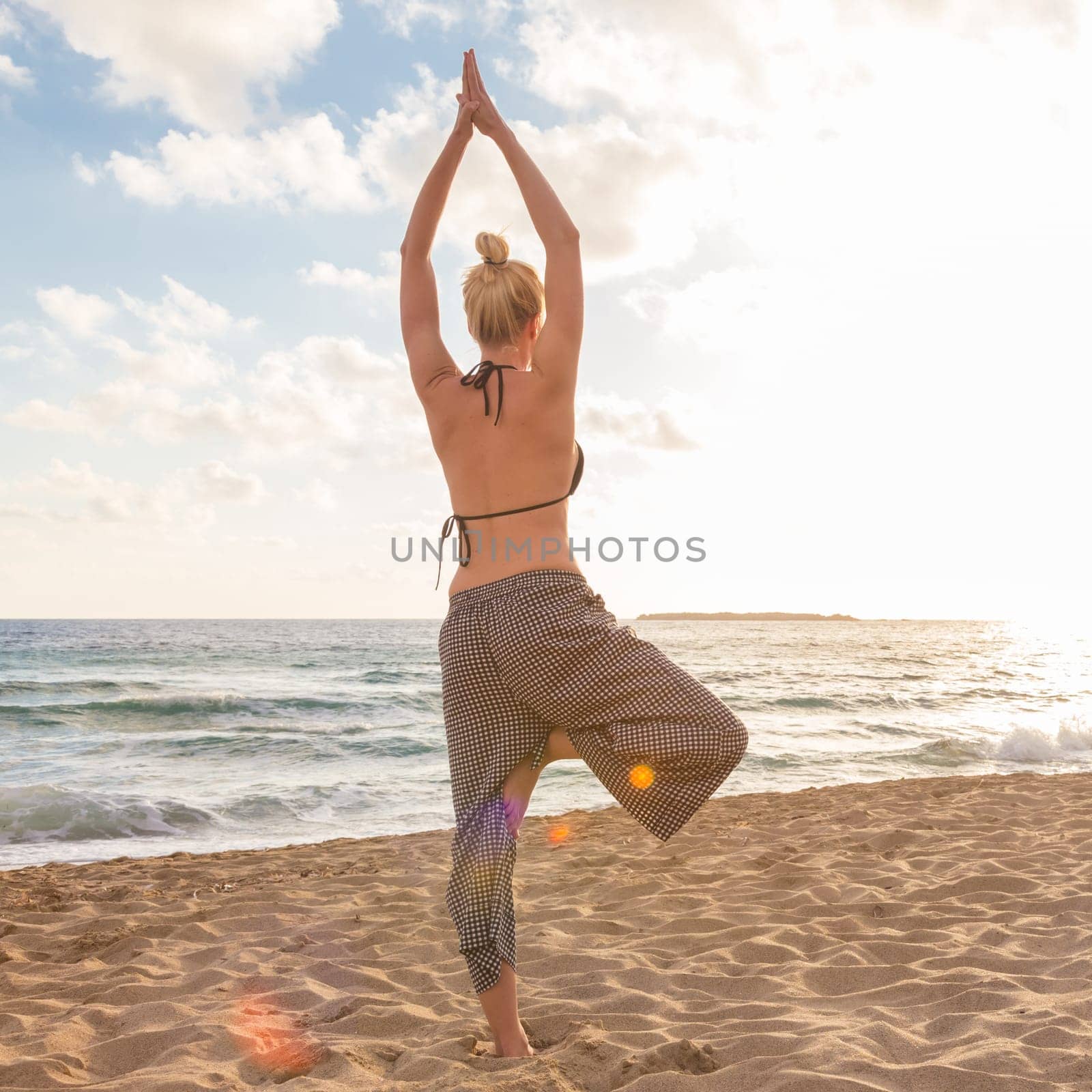 Active young woman practicing yoga on beach at sunset.