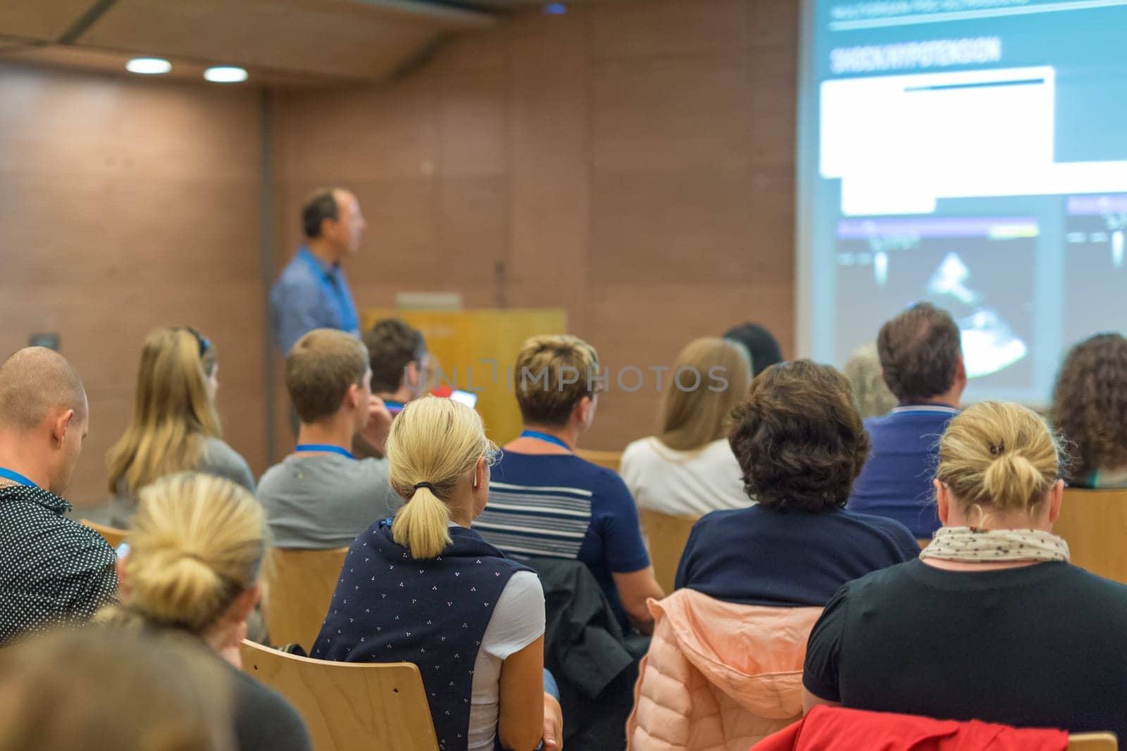 Speaker Giving a Talk at Business Meeting. Audience in the conference hall. Business and Entrepreneurship. Focus on unrecognizable people from rear.