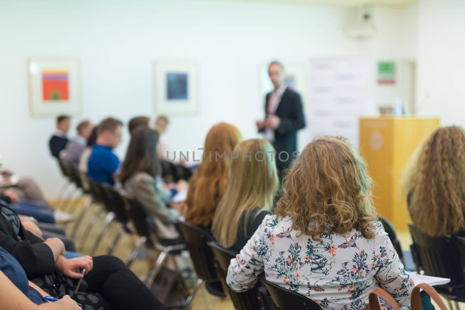 Speaker Giving a Talk at Business Meeting. Audience in the conference hall. Business and Entrepreneurship. Focus on unrecognizable people from rear.